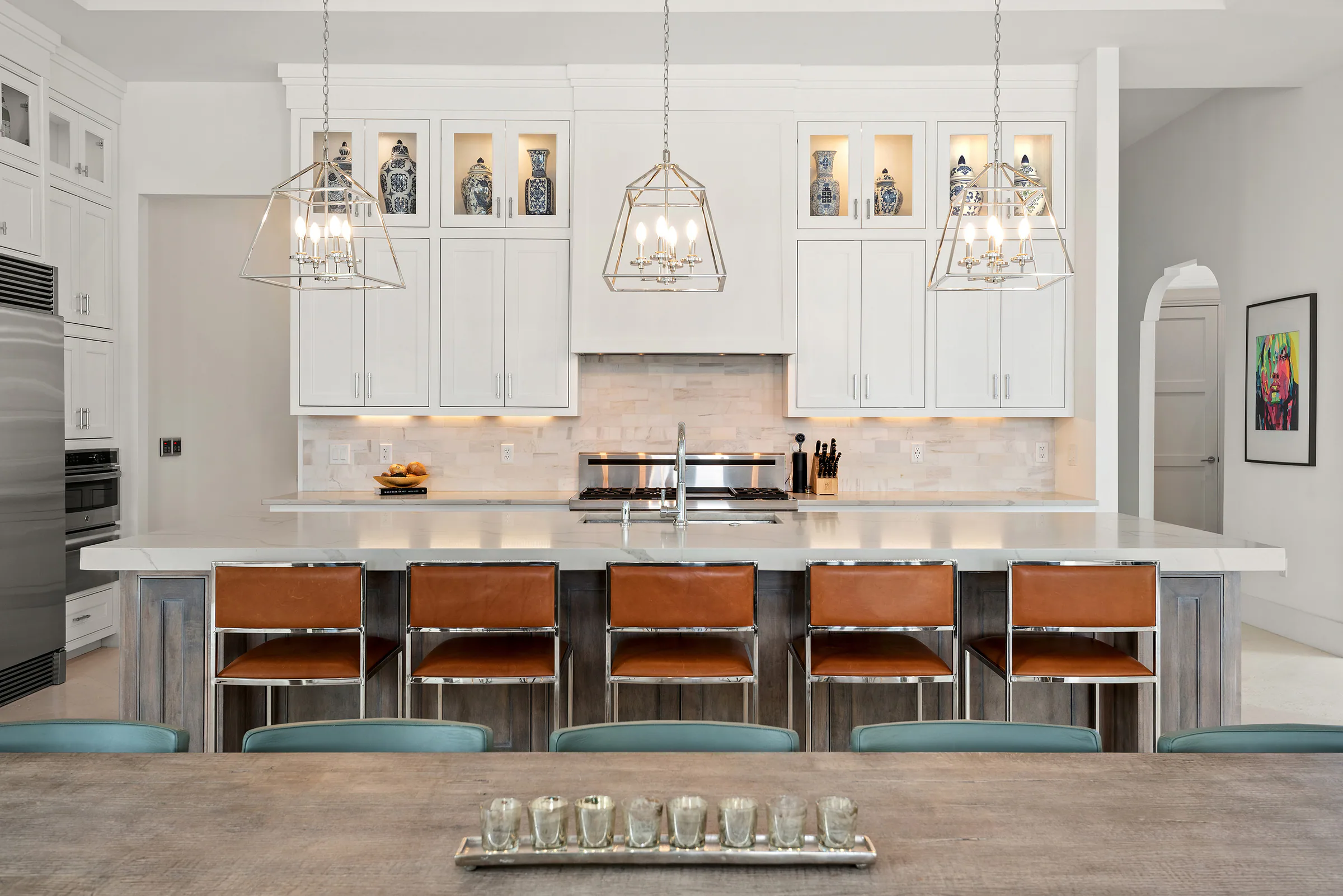 White kitchen with a long island, pendants and wood counter stools.