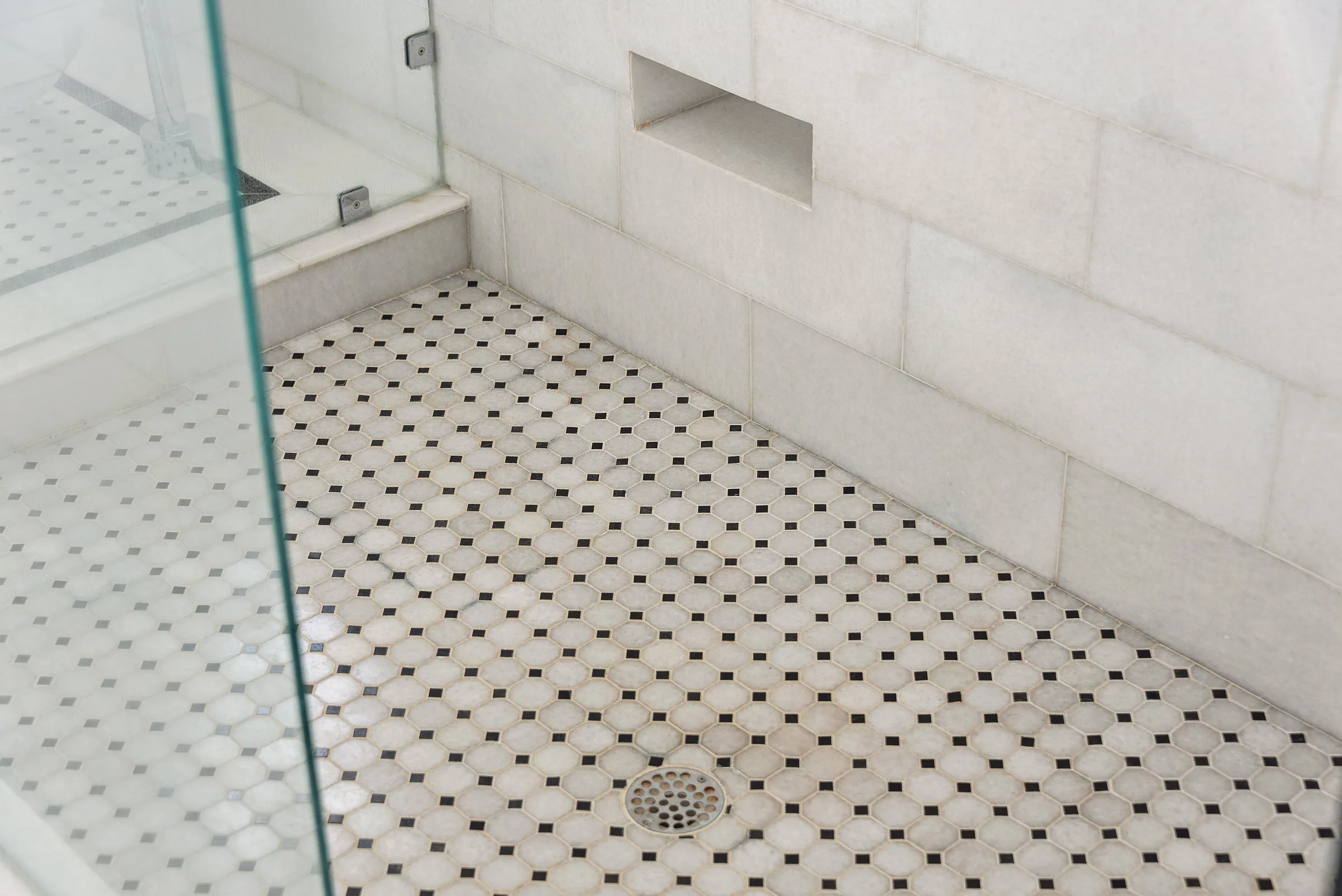 Black-and-white mosaic shower floor and pale tiled walls.