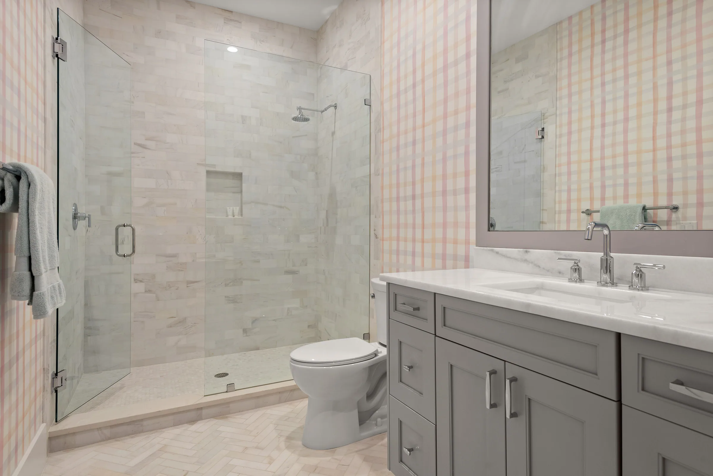 Glass shower and vanity in a pale stone bathroom.