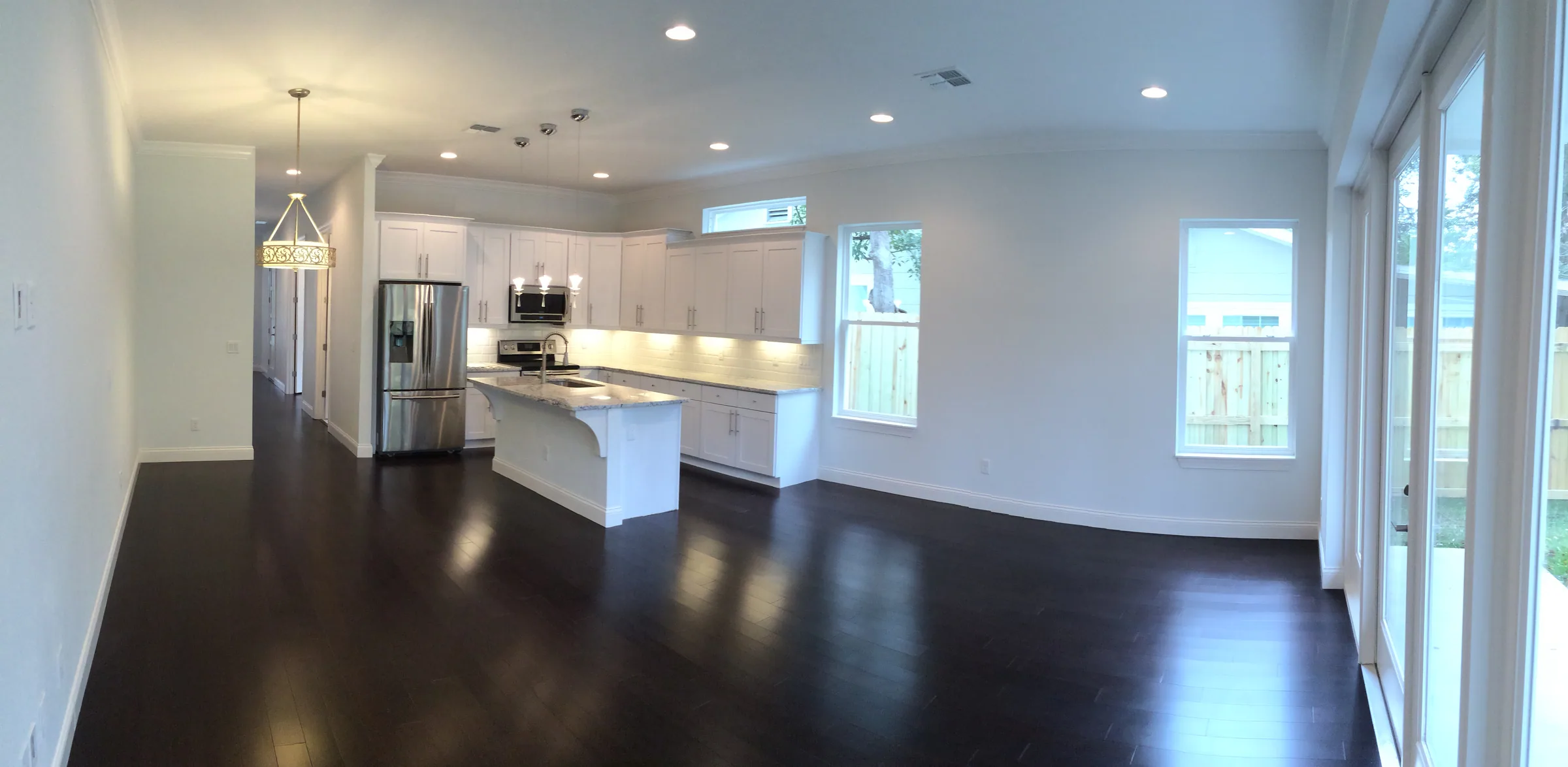 Open Depauw great room and white kitchen with an island, dark flooring and glazed doors.