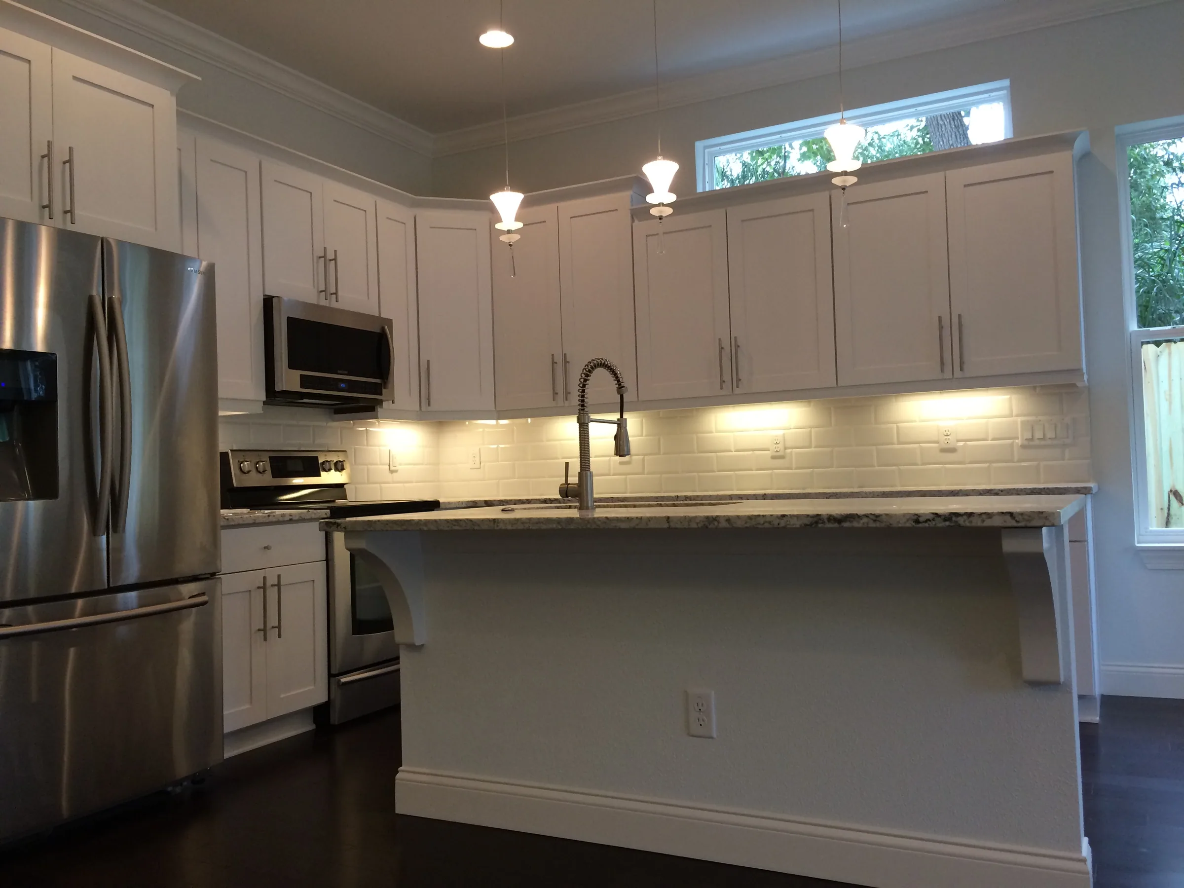 Depauw kitchen with white cabinetry, an island sink, pendant lights and a high horizontal window.