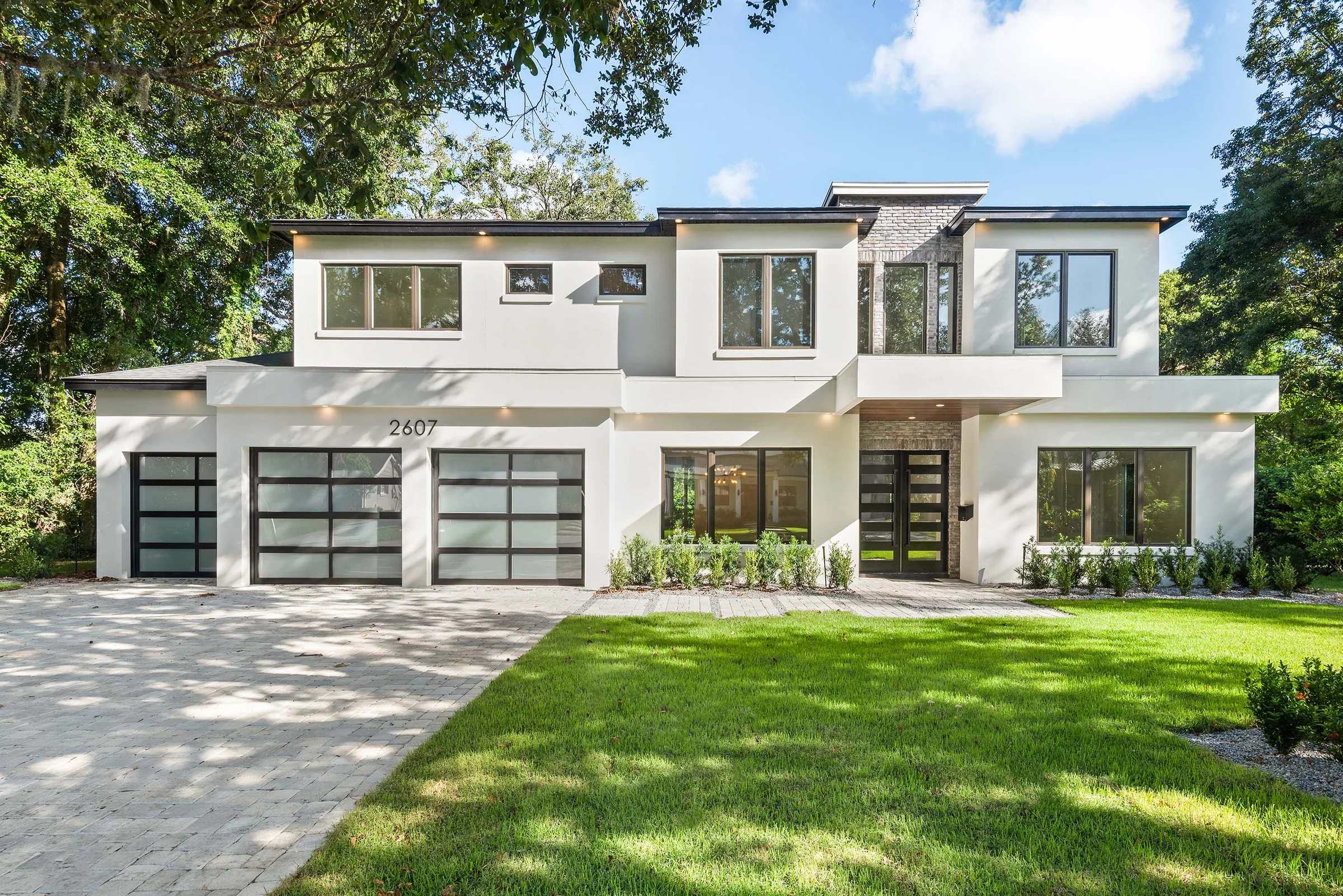 Two-story white home with three glazed garage doors, dark-framed windows and a textured vertical entry accent.