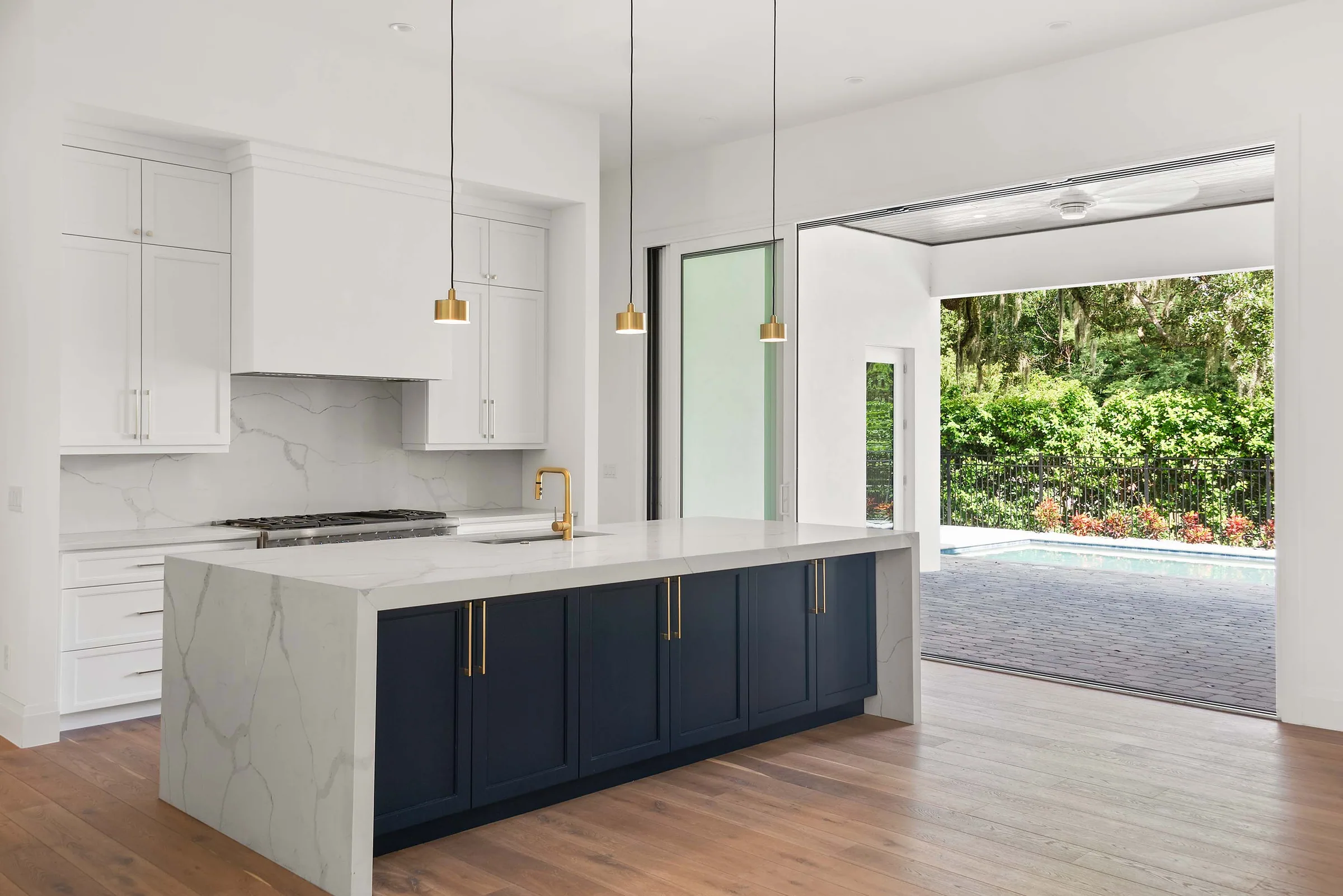 Navy waterfall island beside open sliding glass doors leading to a covered paver patio and pool.