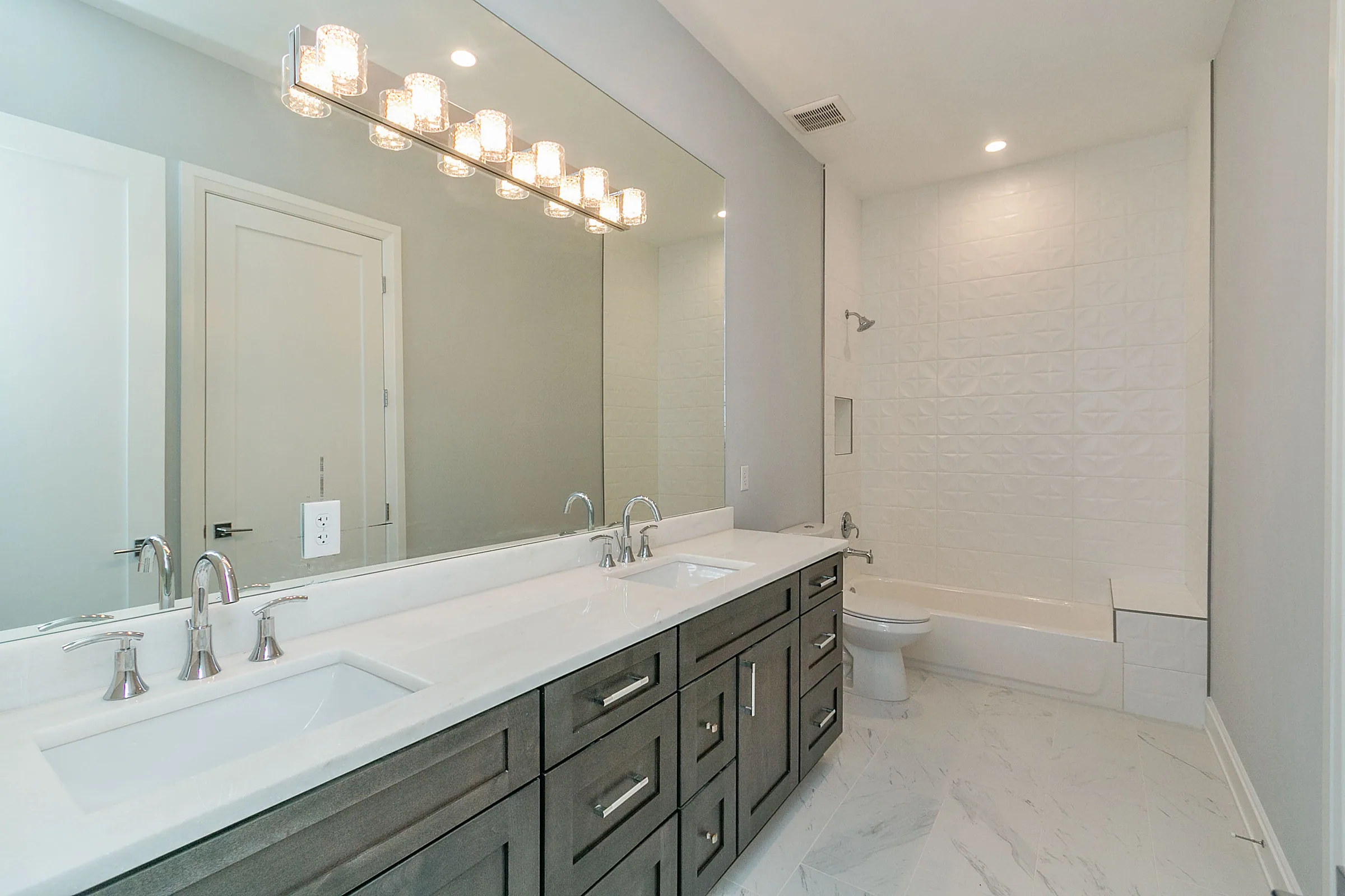 Bright bathroom with a long dark double vanity, broad mirror and pale countertop.