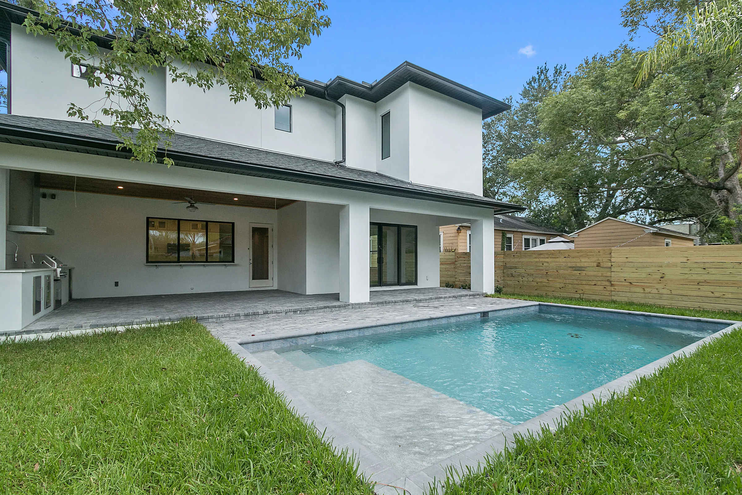 Rectangular pool beside a long covered rear patio, white two-story elevation and lawn.
