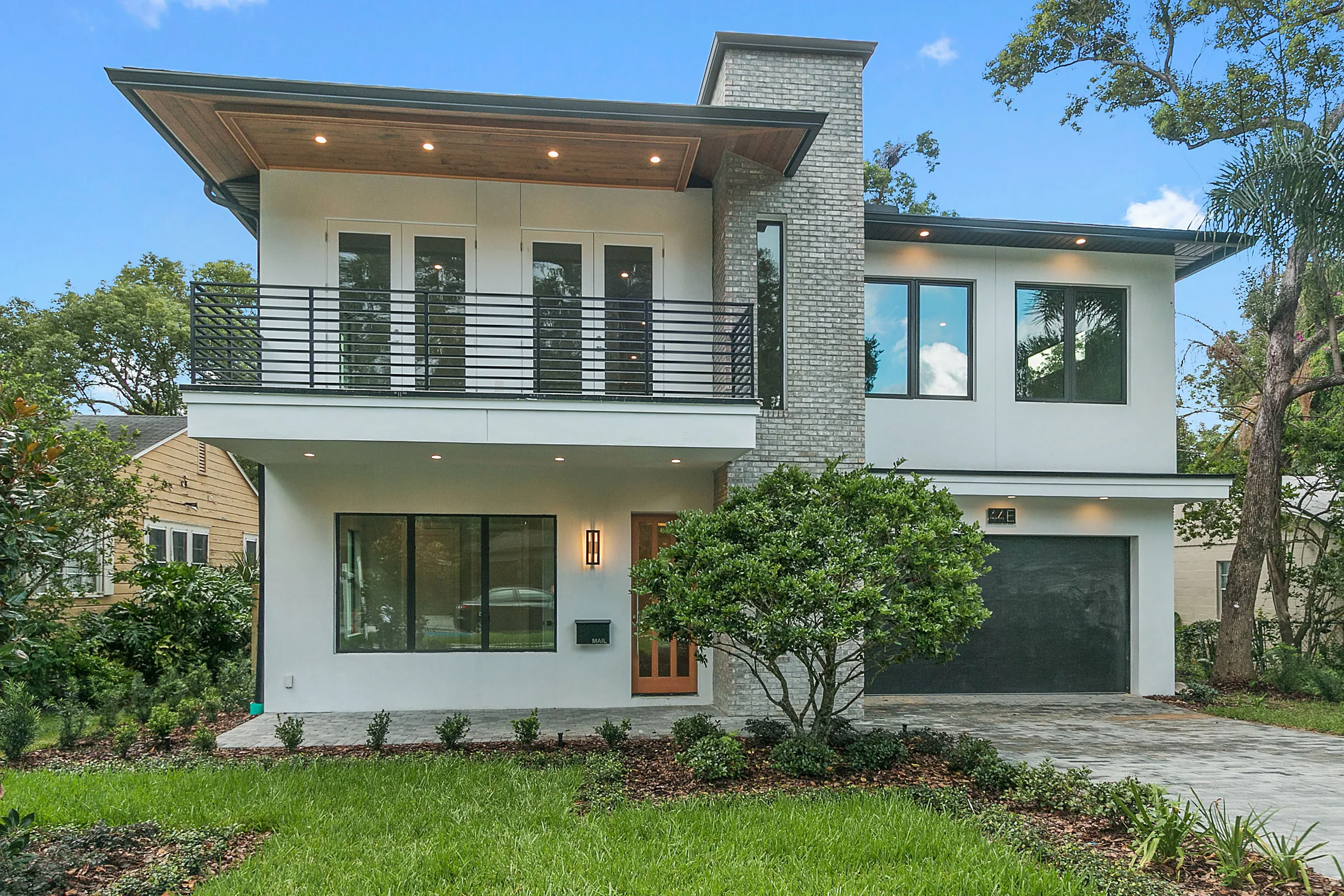 White two-story Vanderbilt residence with a broad upper balcony, horizontal railing, stone entry accent and dark garage door.