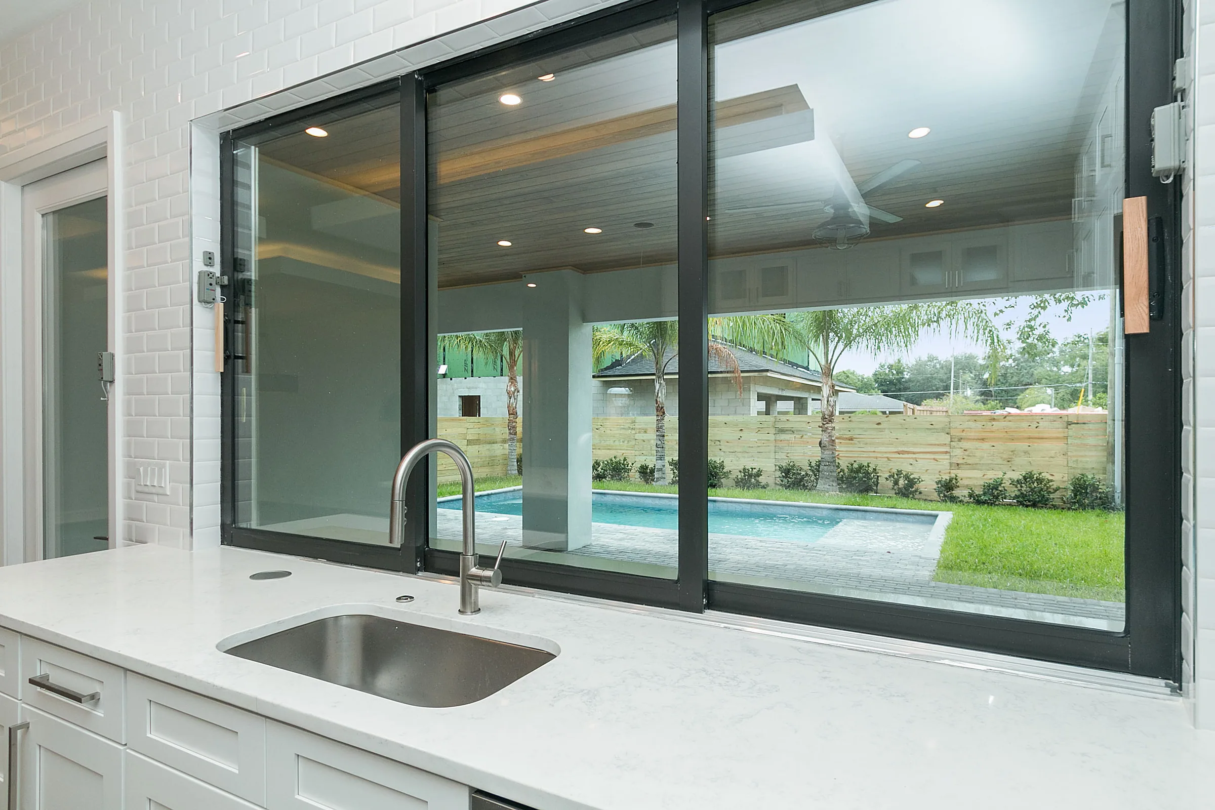 Wide open pass-through above the kitchen sink looking across a covered patio toward the pool and lawn.