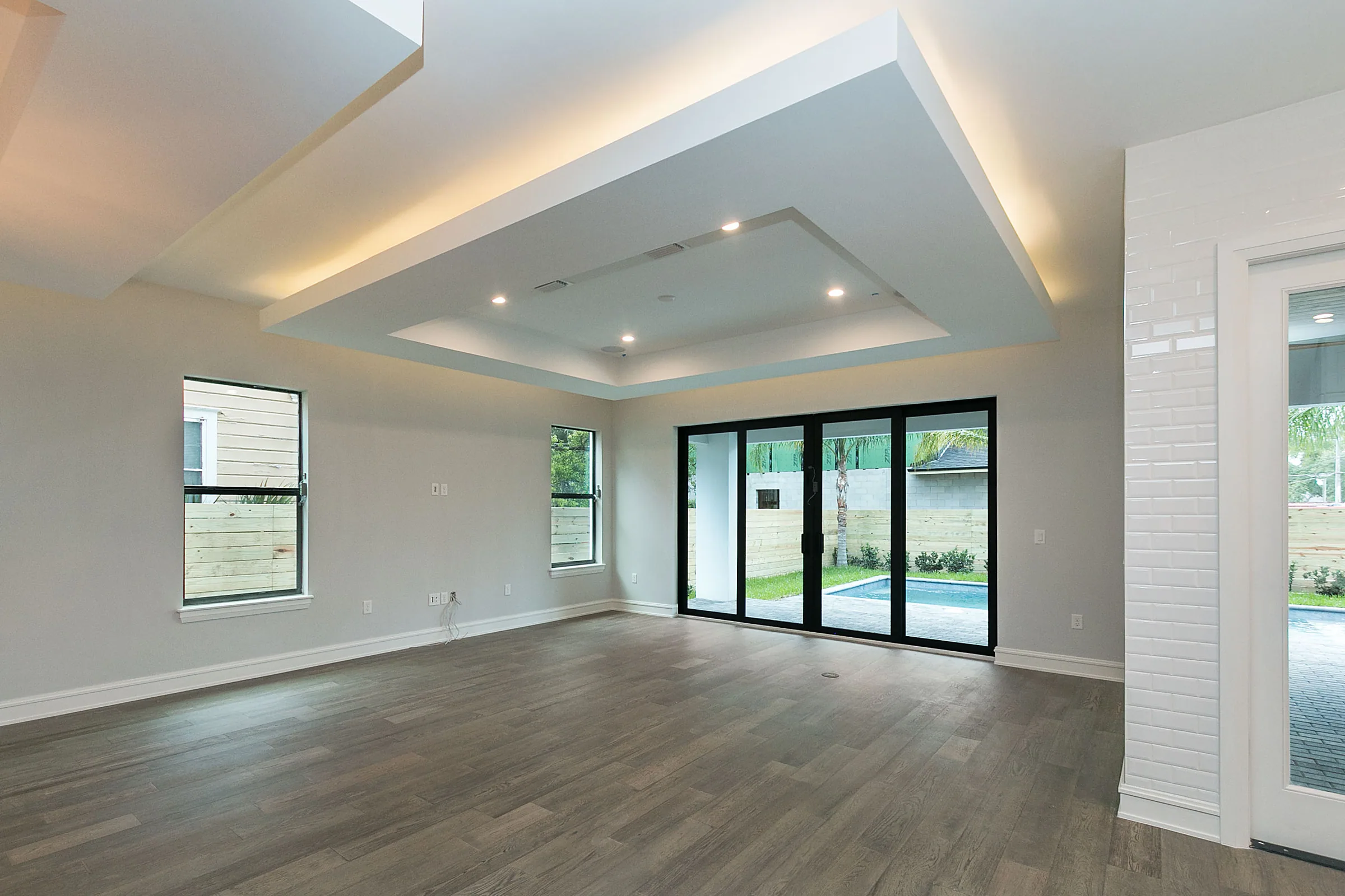 Unfurnished living room with wood-toned flooring, illuminated ceiling recesses and dark-framed sliding doors.
