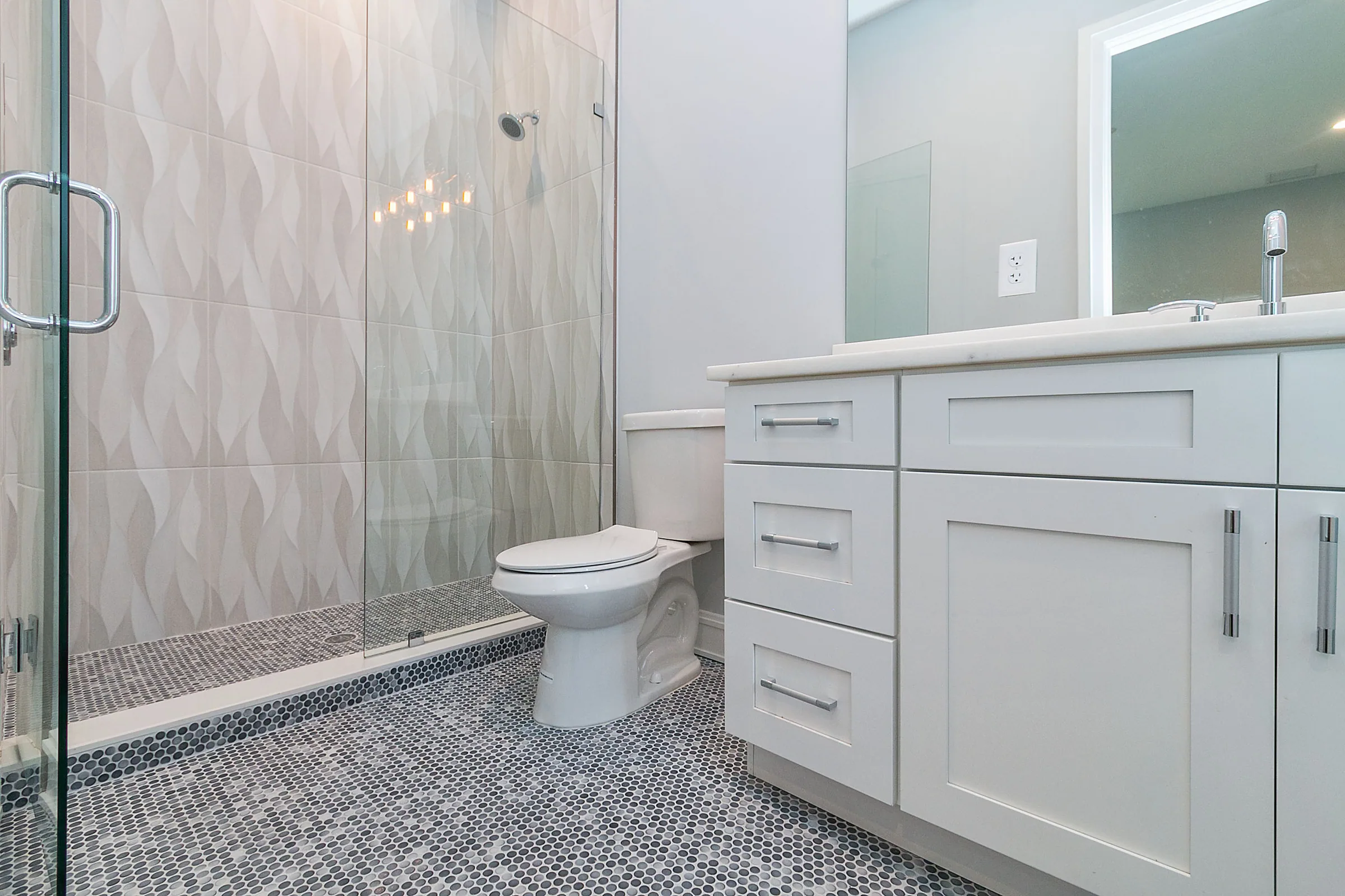 Bathroom with a white vanity, patterned shower wall and small dark mosaic floor tiles.
