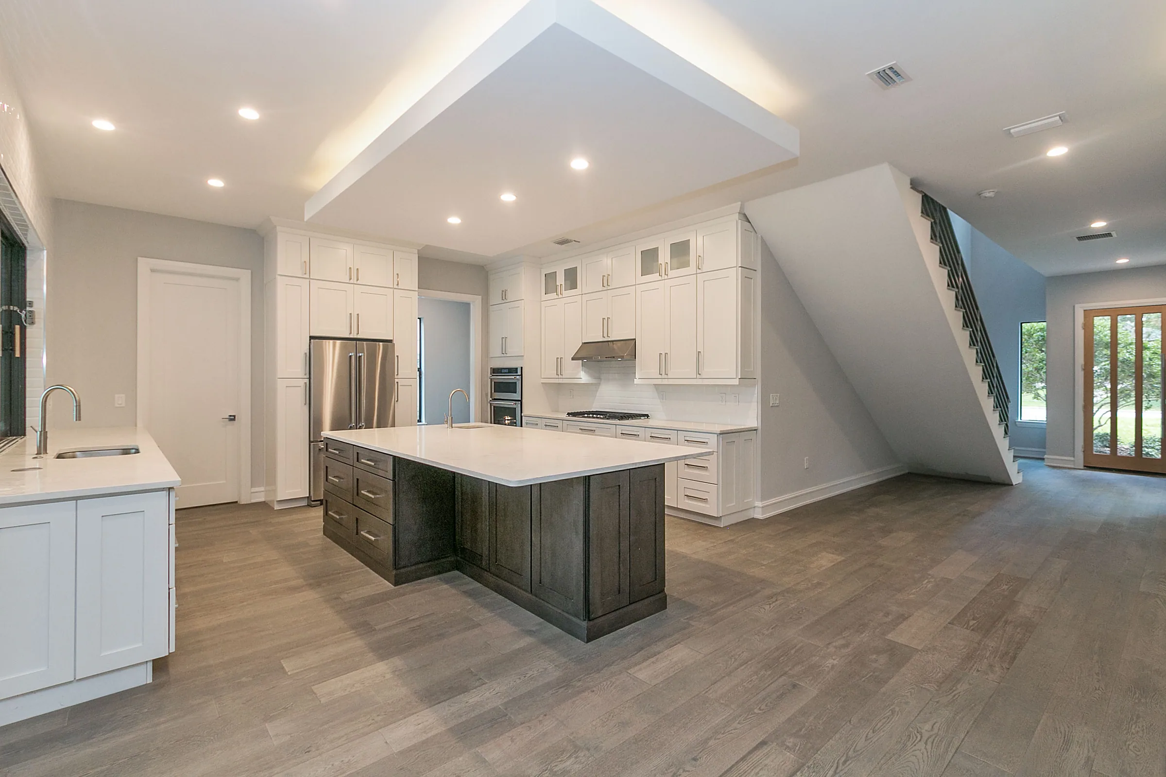 White kitchen cabinets surrounding a dark wood-toned island with a pale countertop beside the open staircase.