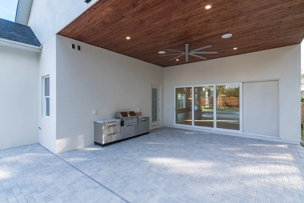 Covered Comstock patio with a wood-toned ceiling, fan, grill cabinetry and sliding doors to the house.
