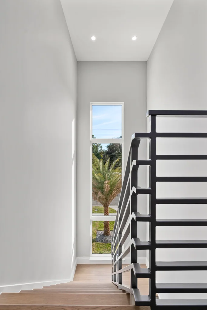 Comstock stair with wood-toned treads, dark horizontal railing and a tall window overlooking a palm.