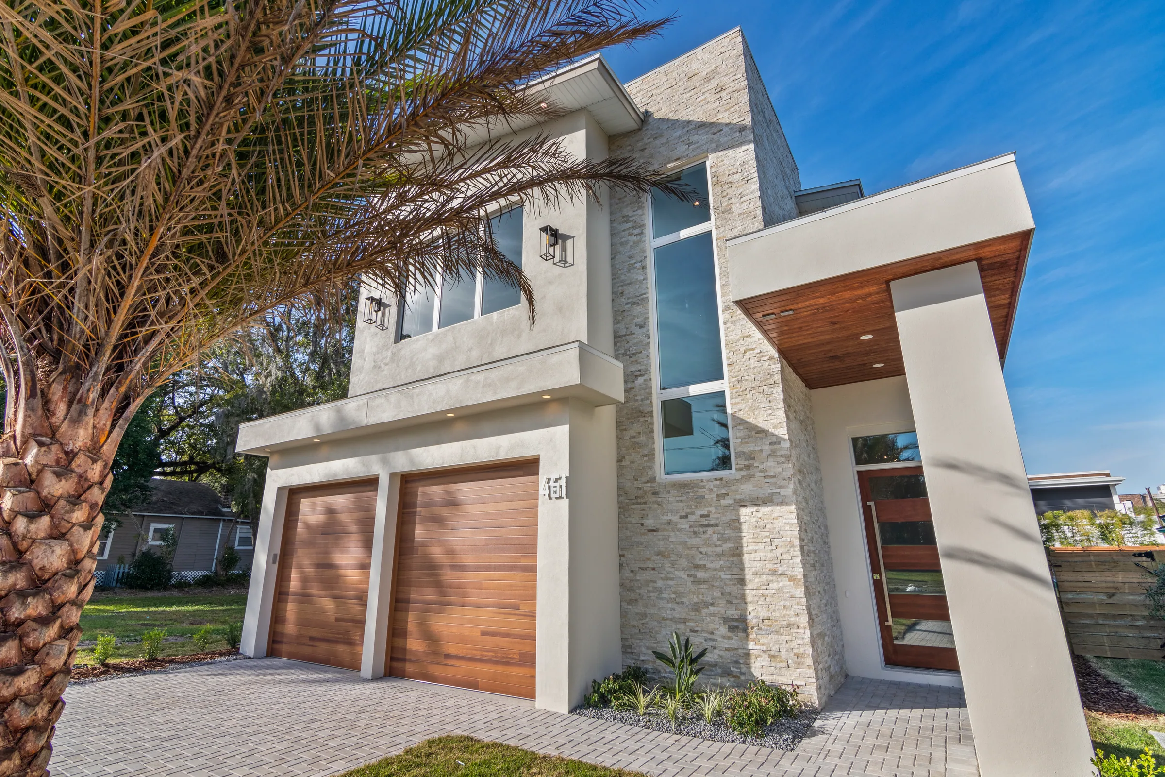 Two-story Comstock facade with tall entry glazing, light textured cladding and wood-toned garage doors.