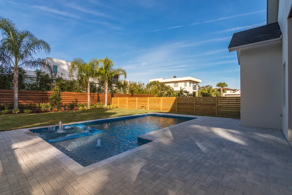 Comstock backyard pool with a raised square basin, paver terrace, lawn and horizontal wood fencing.