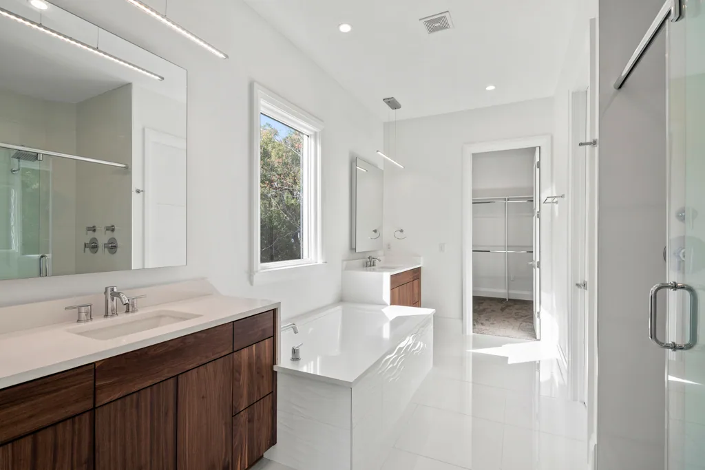 Comstock bathroom with wood-toned vanities, a rectangular bathtub and a glass shower enclosure.
