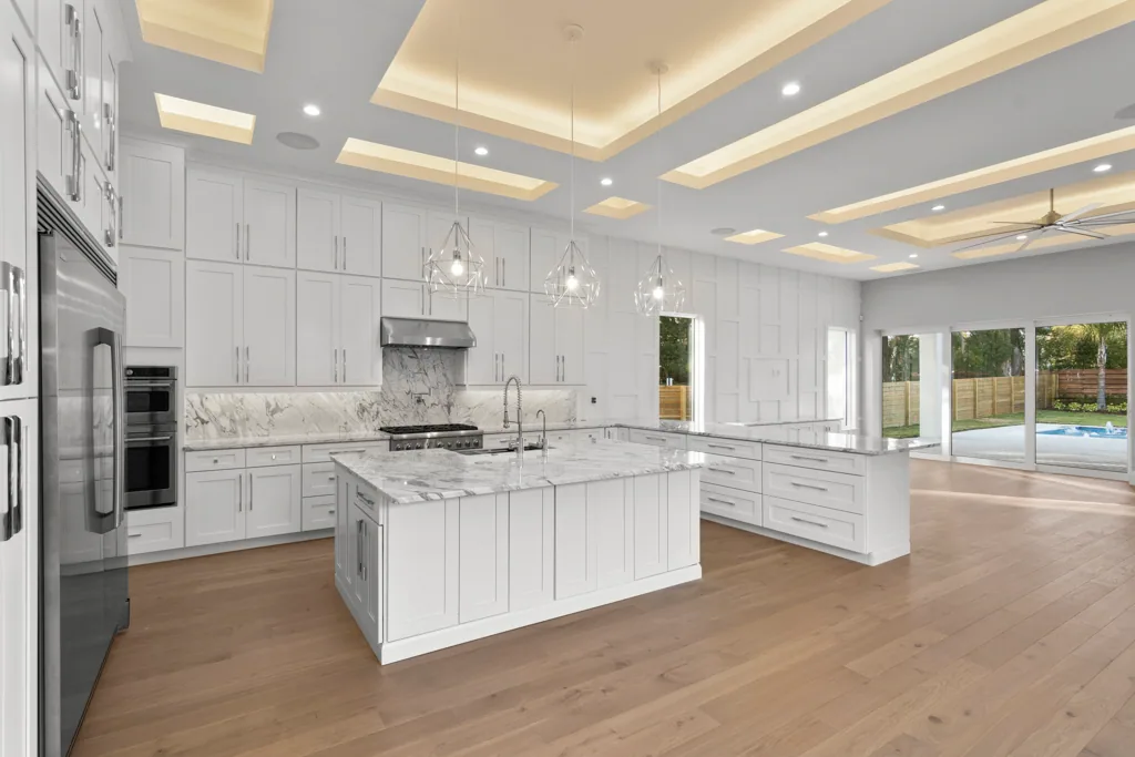 White Comstock kitchen with a veined island, geometric pendant lights and an illuminated ceiling grid.