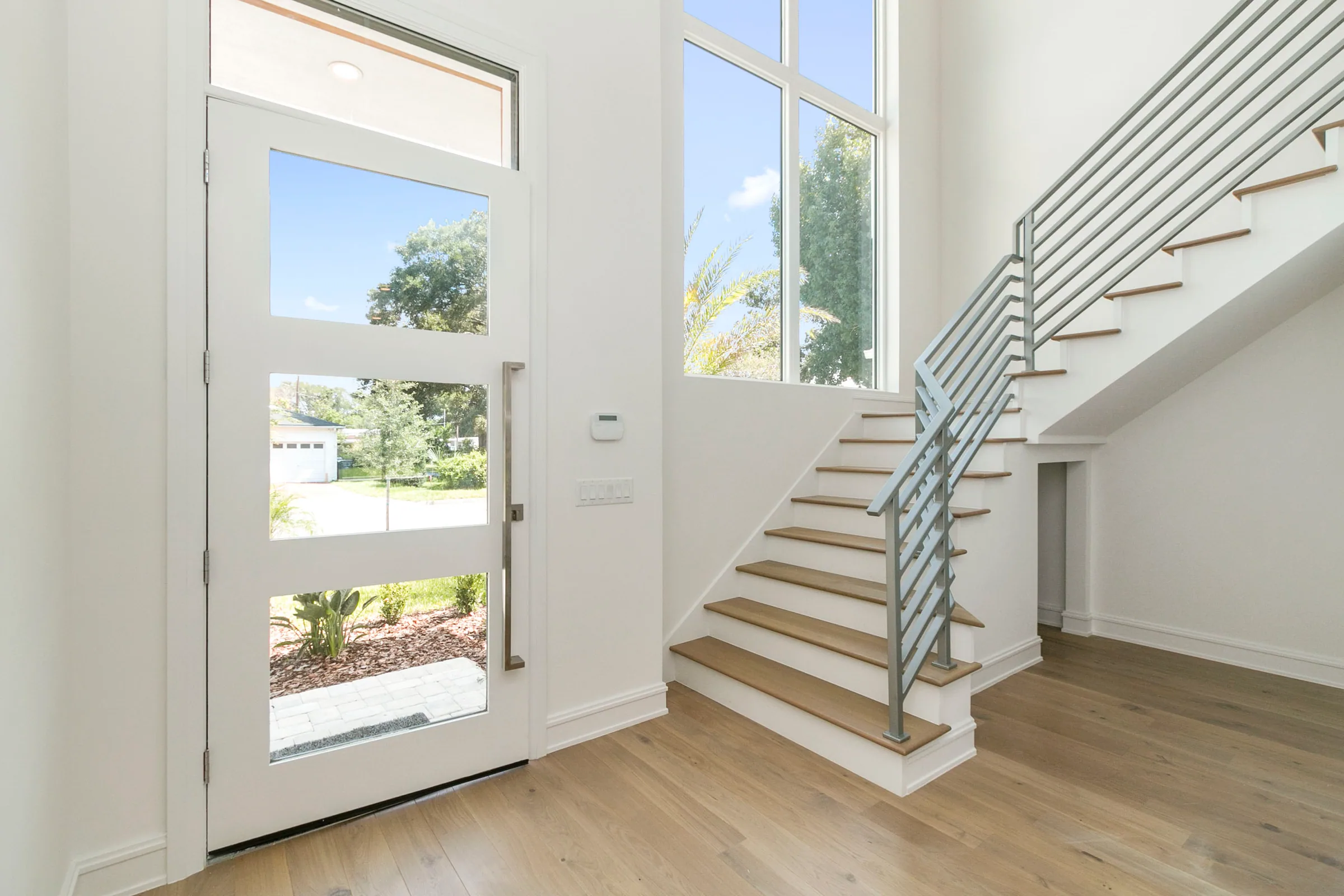 Wood-tread staircase with horizontal metal railings beside a tall window and glazed front door.