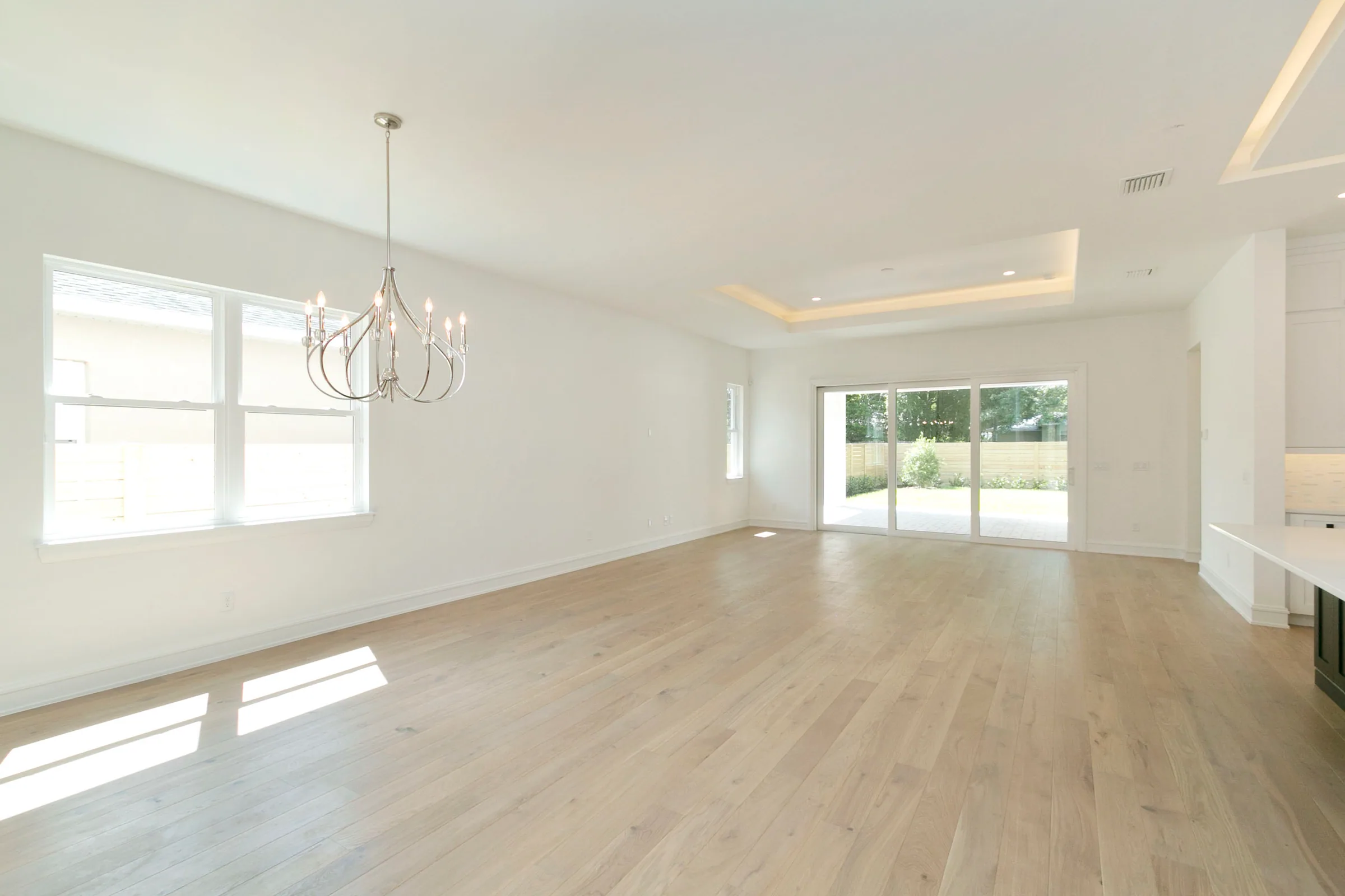 Open living and dining area with pale plank floors, a chandelier and wide sliding glass doors to the rear porch.