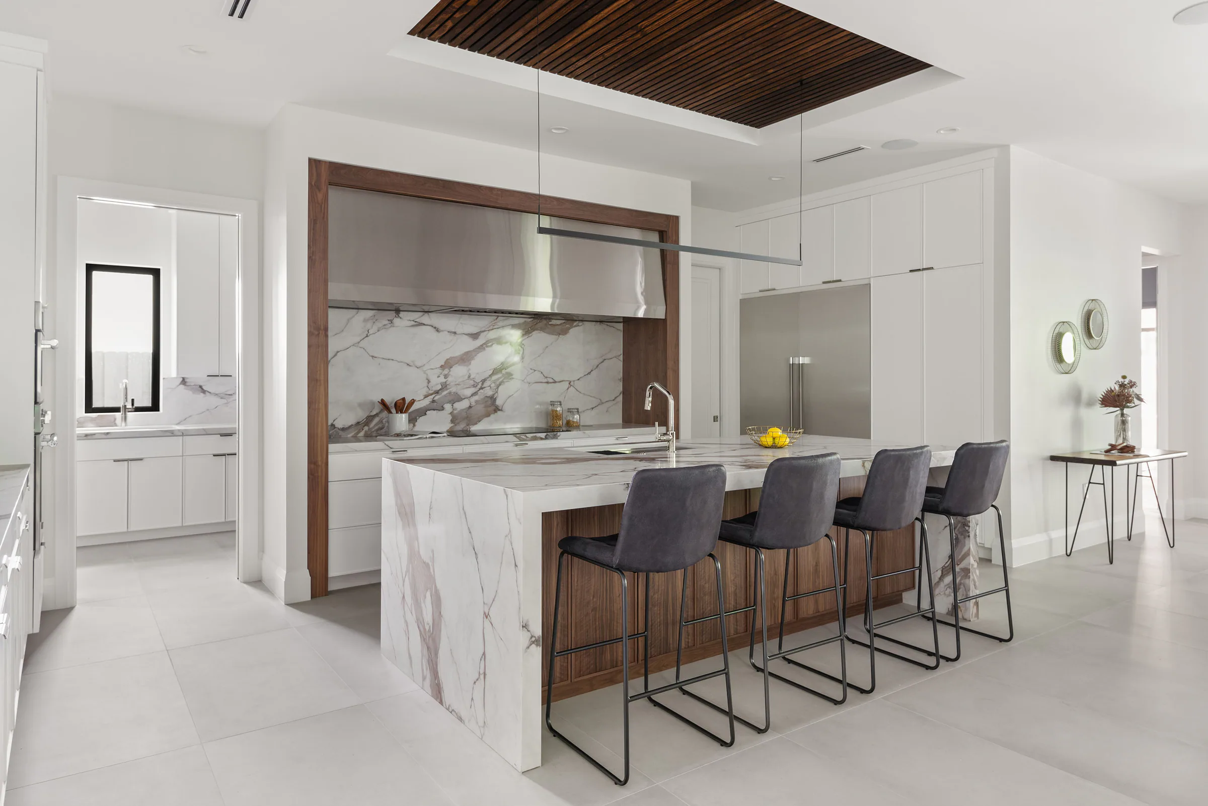 Marble waterfall island with dark upholstered counter stools. New Hampshire, a custom home by Rare Builders in Orlando.