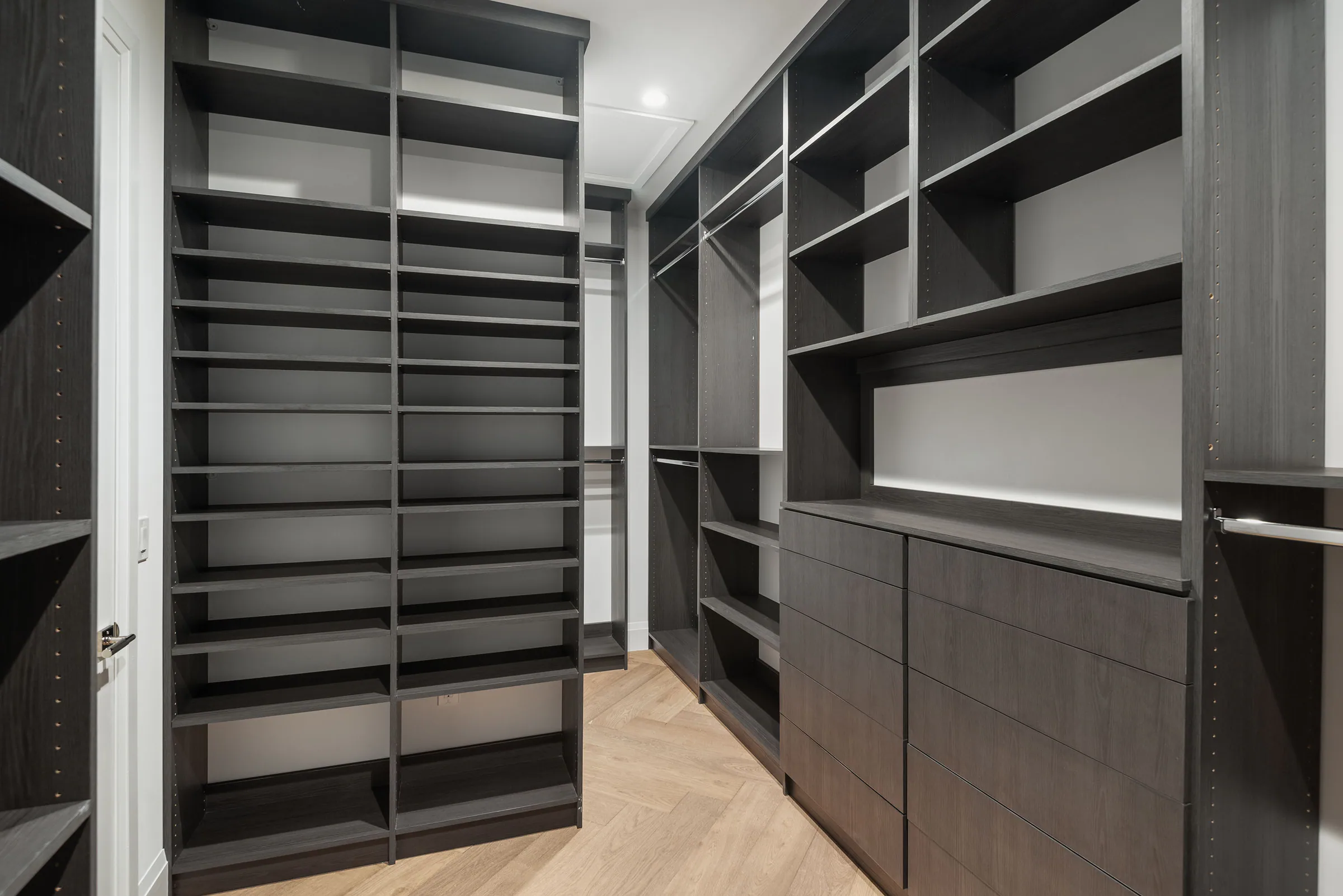 Walk-in closet with dark open shelving and built-in drawers.