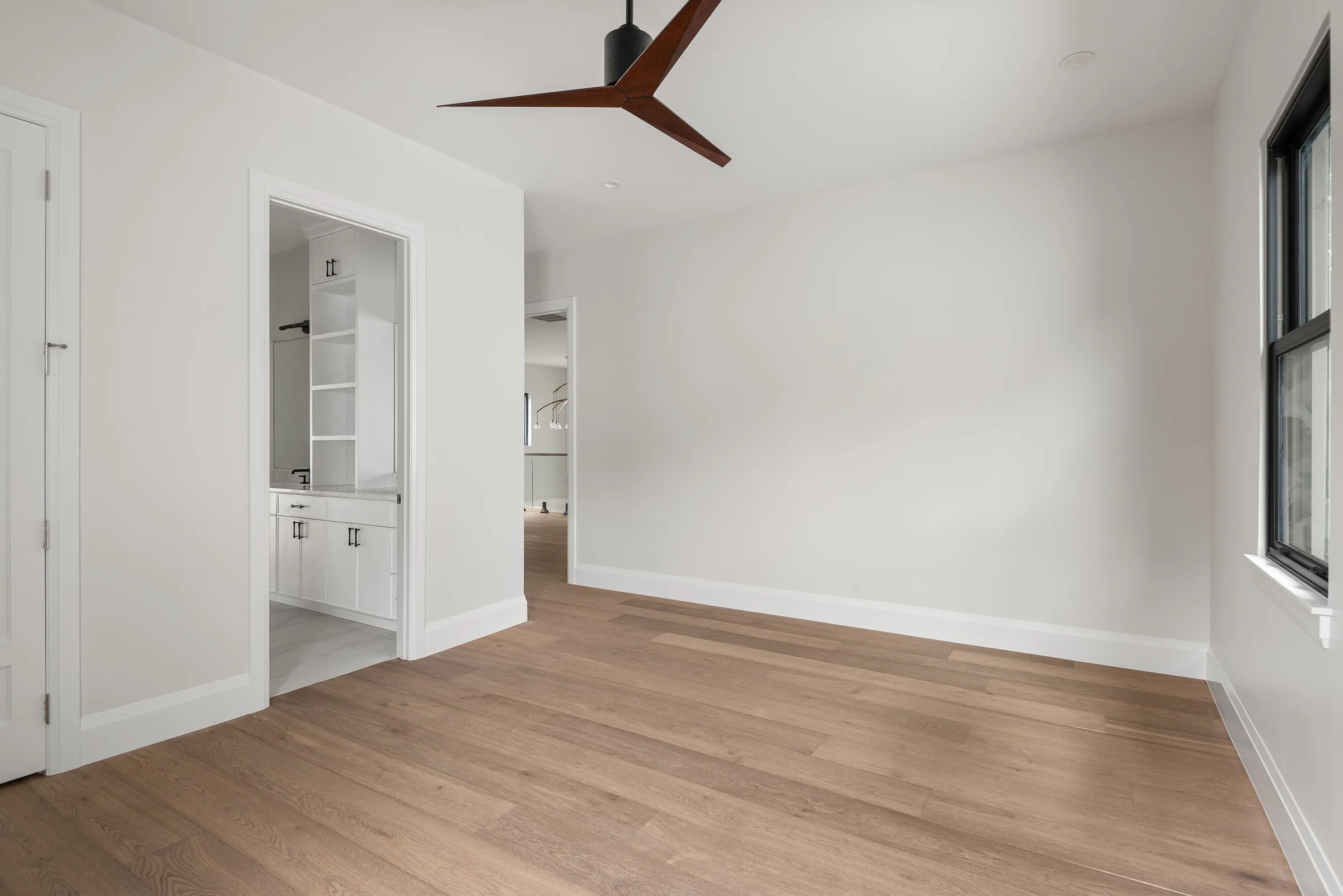 Unfurnished bedroom with pale wood floor and dark ceiling fan.