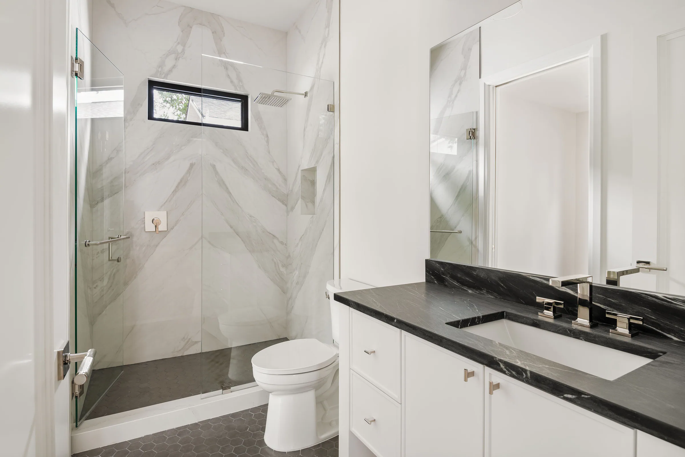 White bath with dark vanity and glass shower.