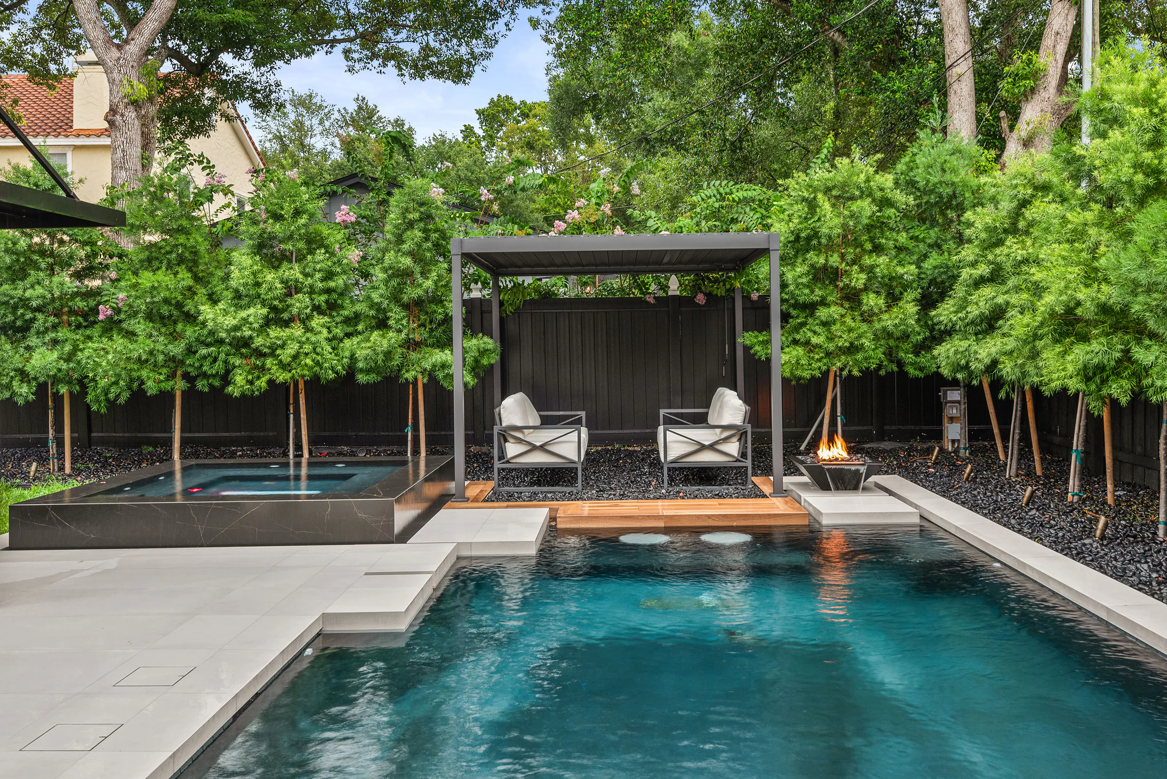 Rectangular pool framed by dark cabanas and mature trees. New Hampshire, a custom home by Rare Builders in Orlando.