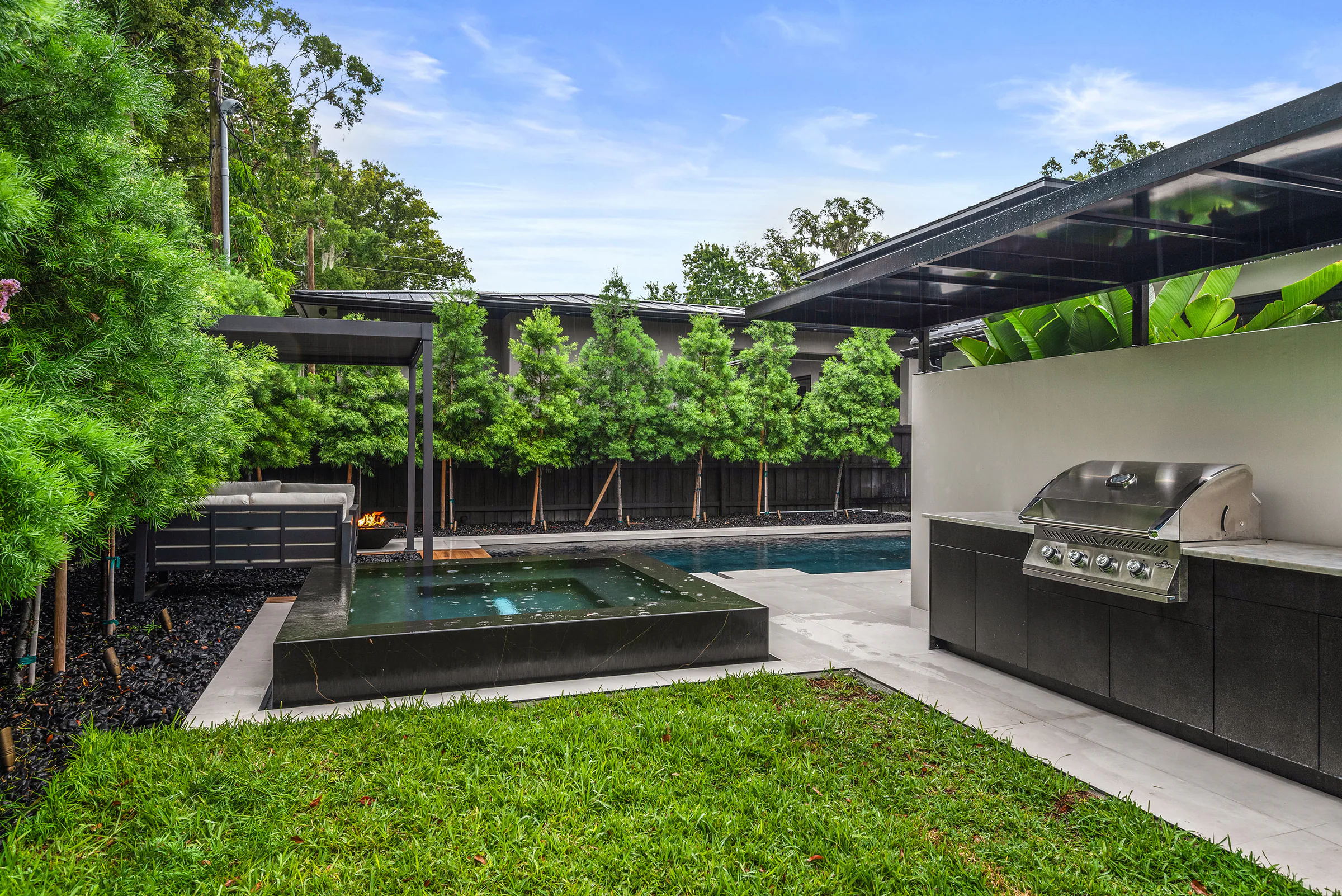 Pool, lawn and outdoor fireplace beneath dense planting.