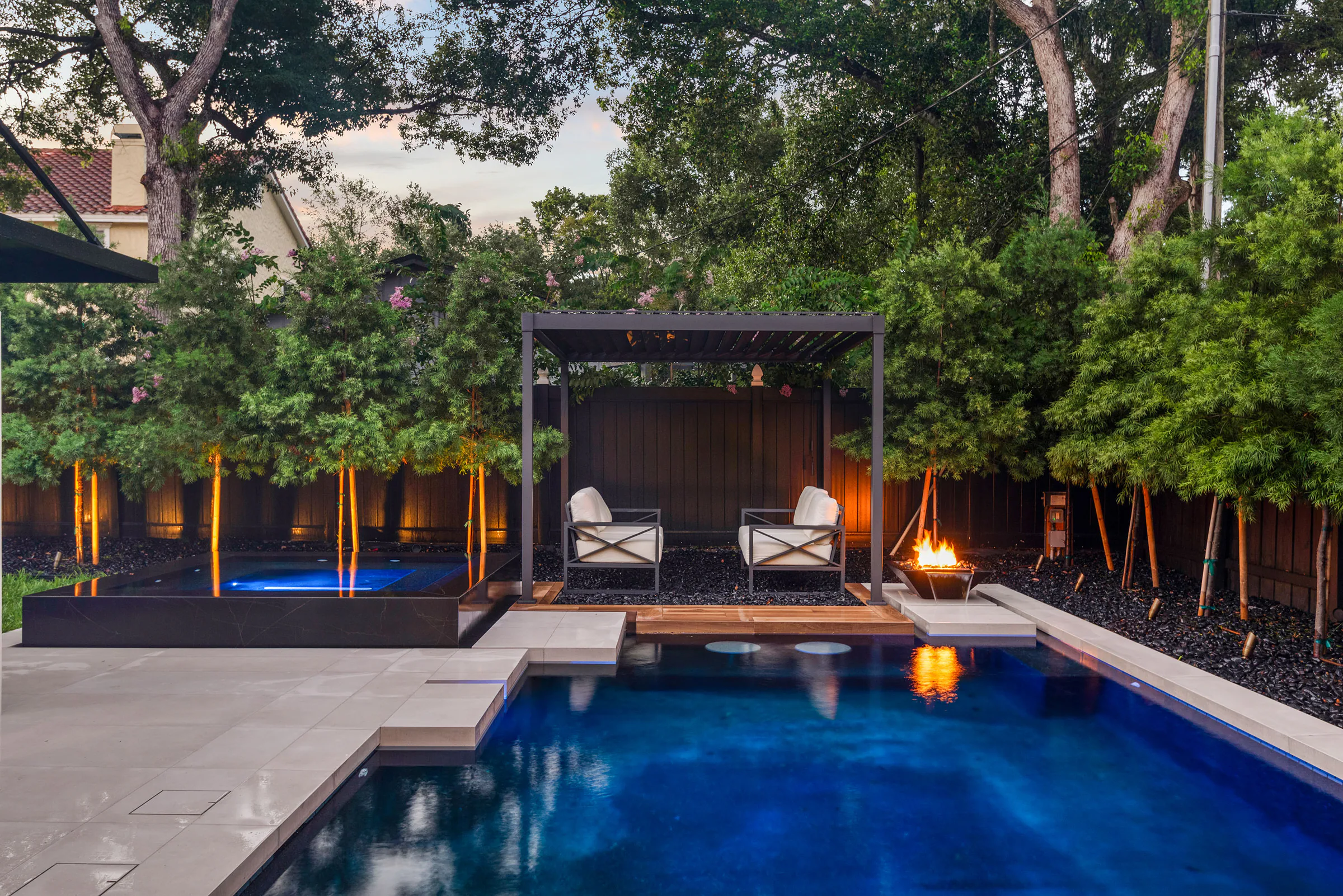 Pool illuminated blue beneath the dark cabana. New Hampshire, a custom home by Rare Builders in Orlando.