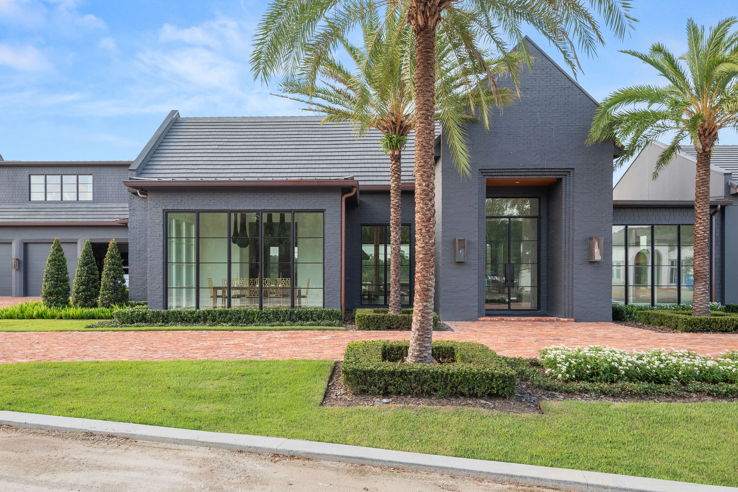 Street view of Manor showing the dark brick wings, central gabled entry, palms and brick drive.