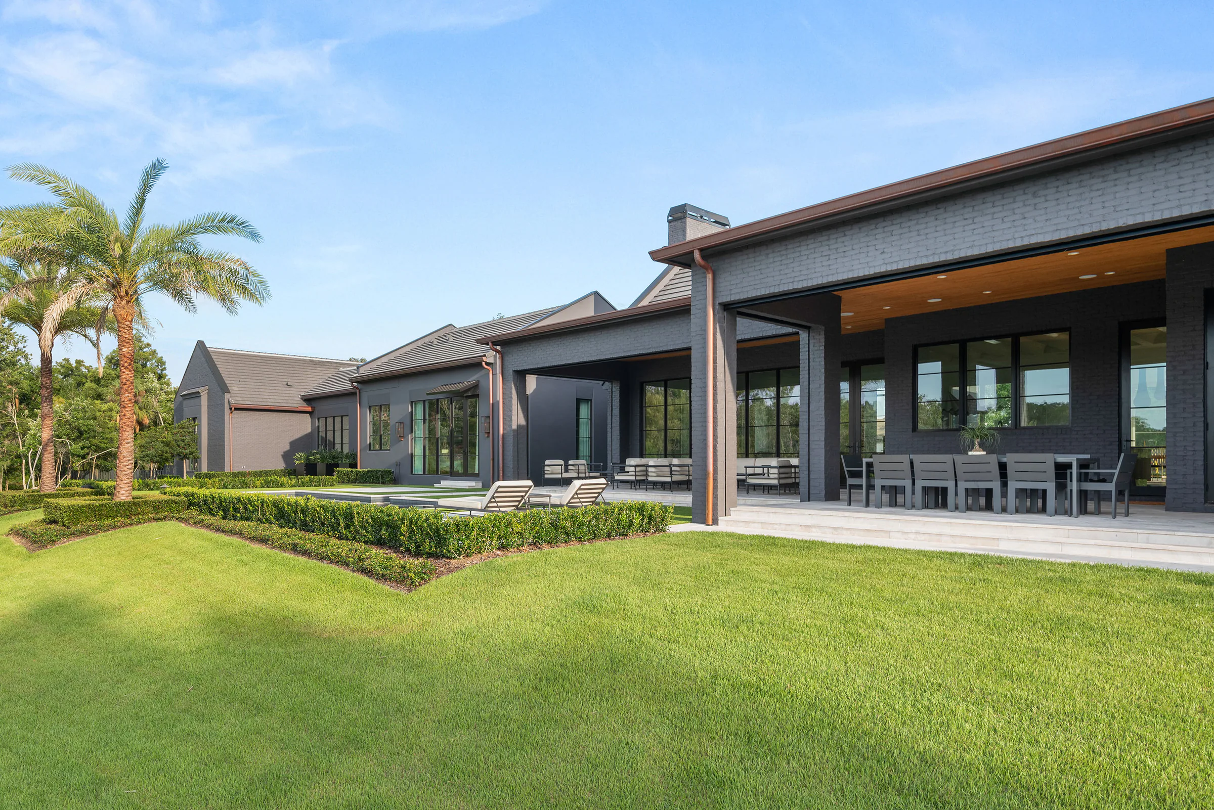 Rear lawn view toward Manor's covered terrace, dark brick walls and broad glazed openings.