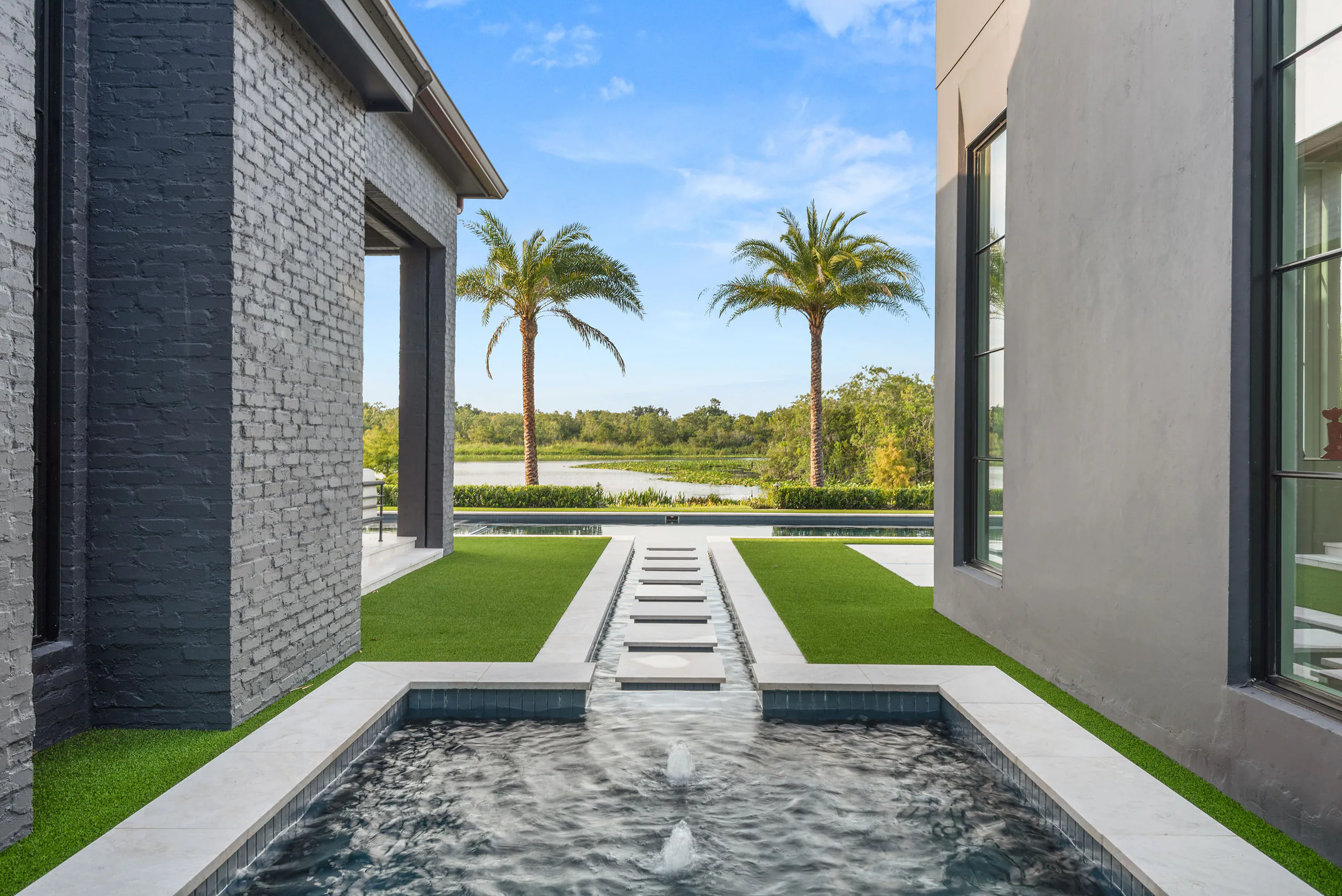 Covered passage framing stepping stones across a shallow water feature toward the pool and palms.