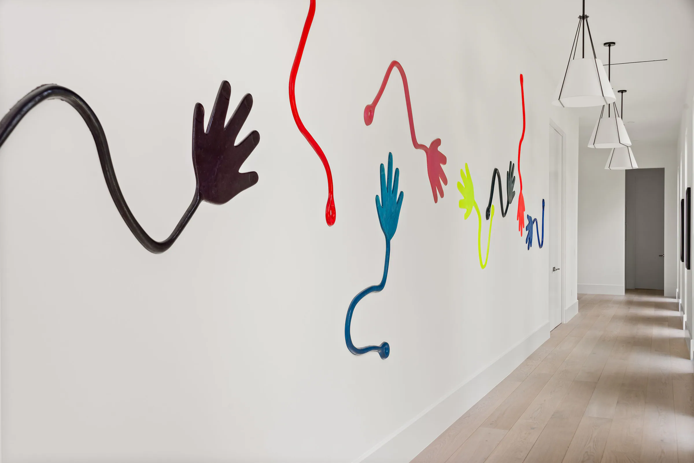 White gallery hallway animated by colorful hand-shaped wall lines and a row of pendant lights.