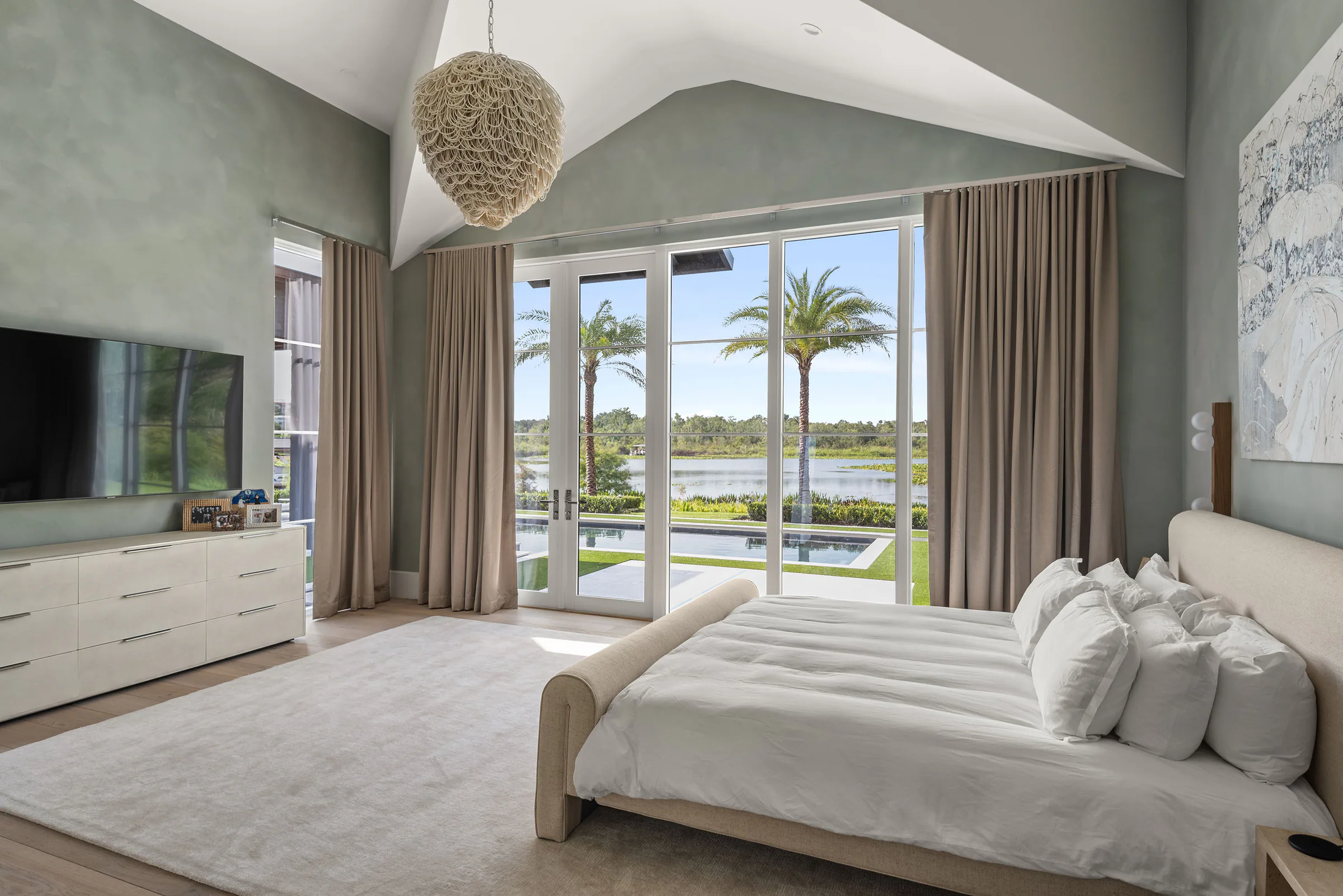 Bedroom with soft green walls, a white upholstered bed and sliding glass doors opening toward the pool.