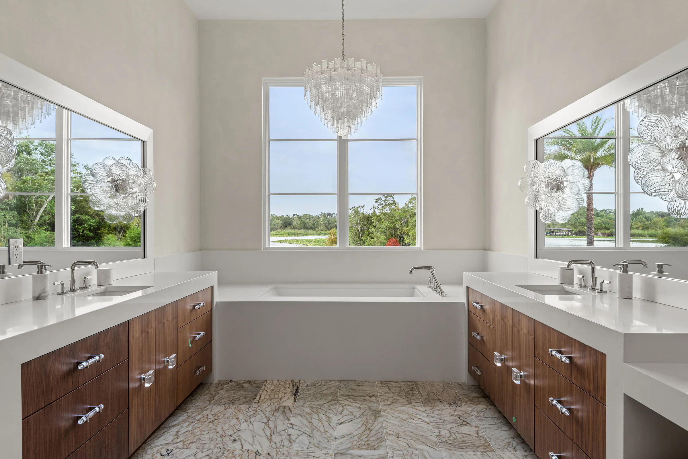 Primary bathroom with twin wood vanities, broad mirrors, a freestanding tub and garden views.