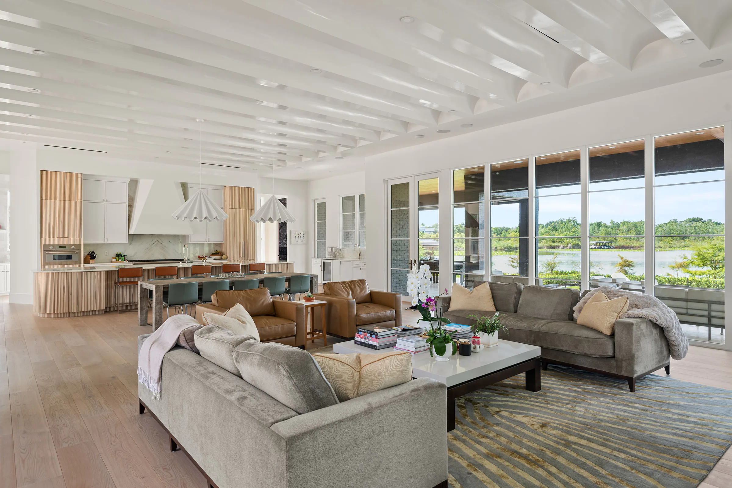 Open living room with pale oak flooring, exposed white ceiling beams and wide lake-facing windows.