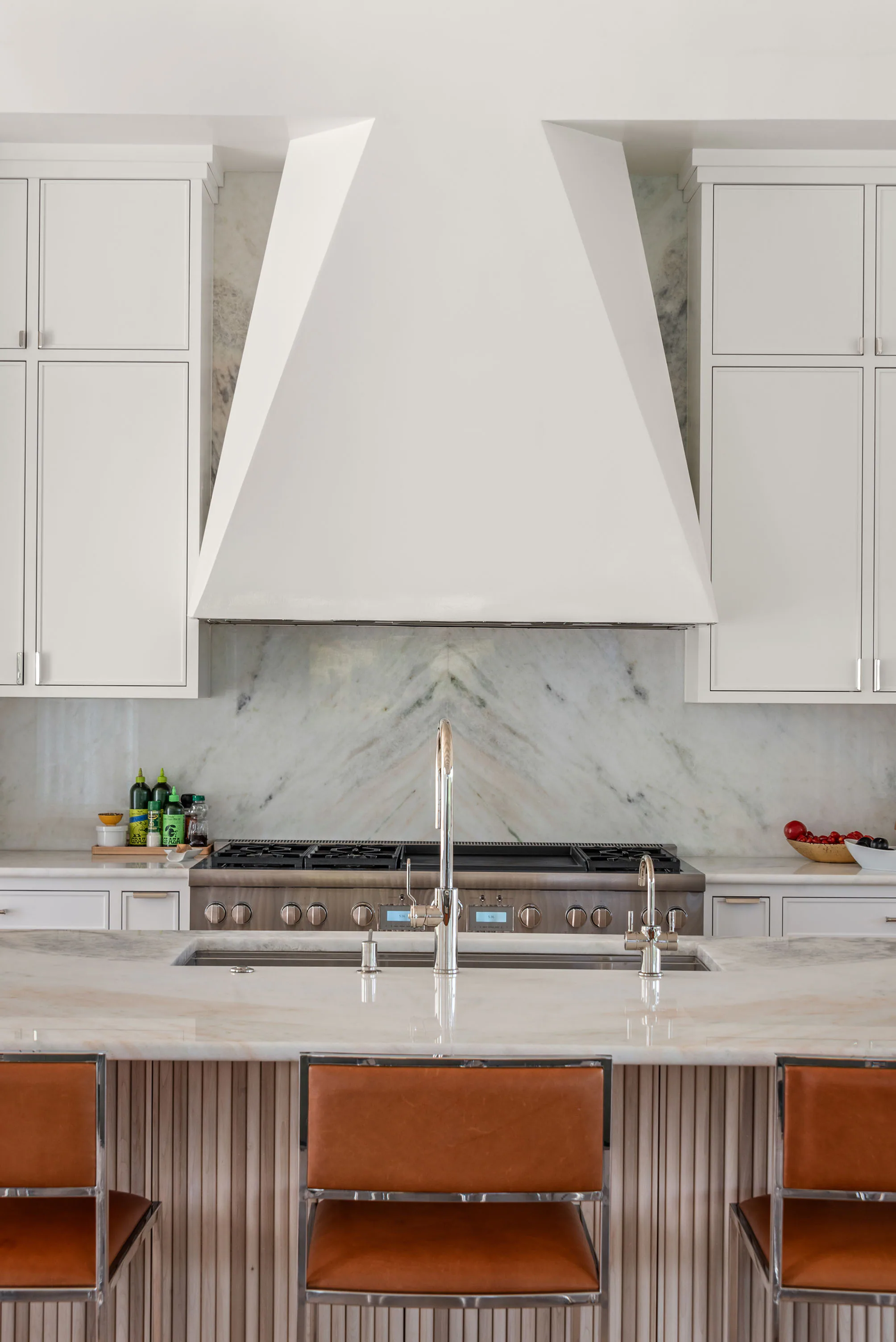 Vertical detail of the white plaster range hood, marble backsplash and wood counter stools.
