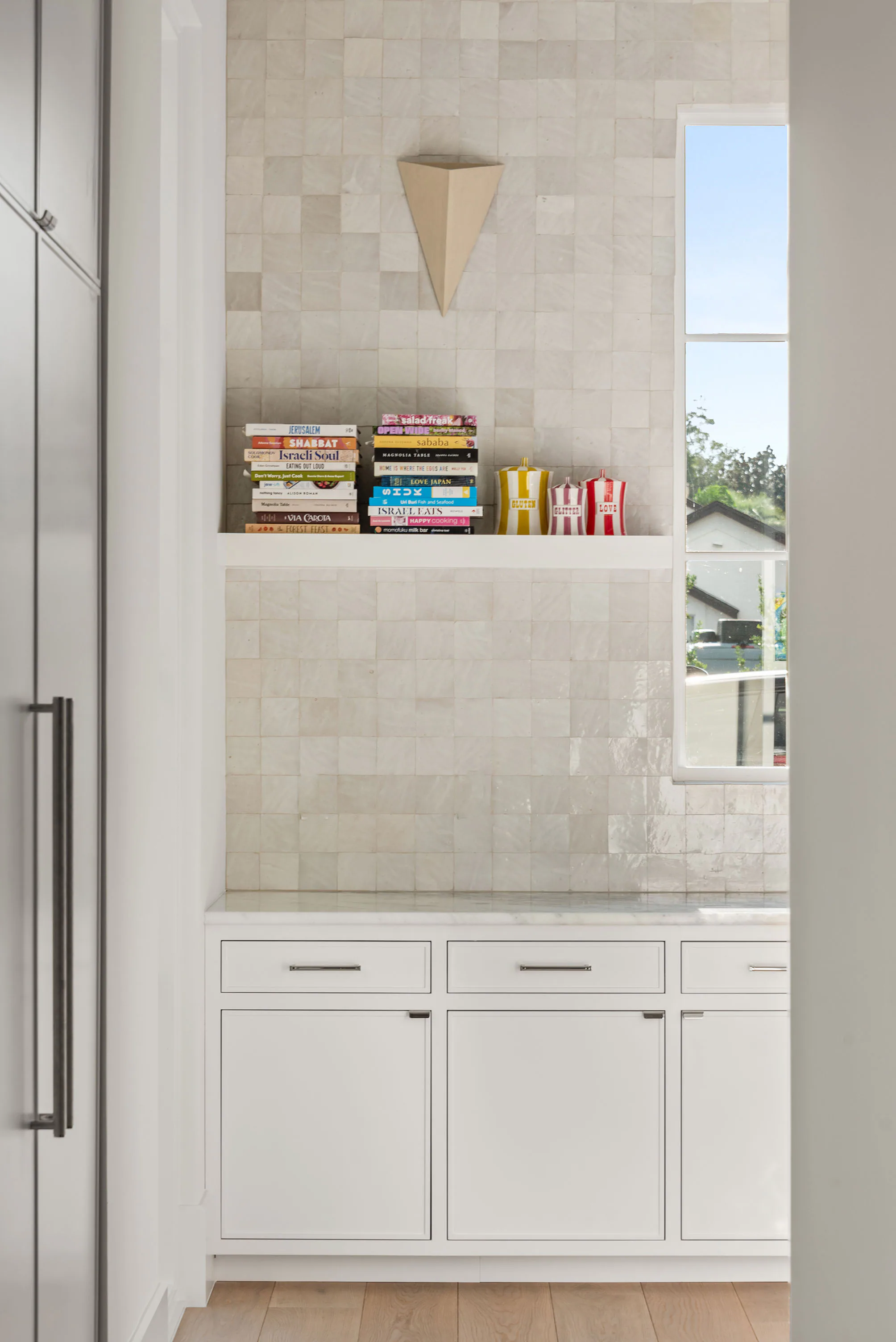 Built-in cabinet alcove finished with pale patterned tile, open shelves and a small window.