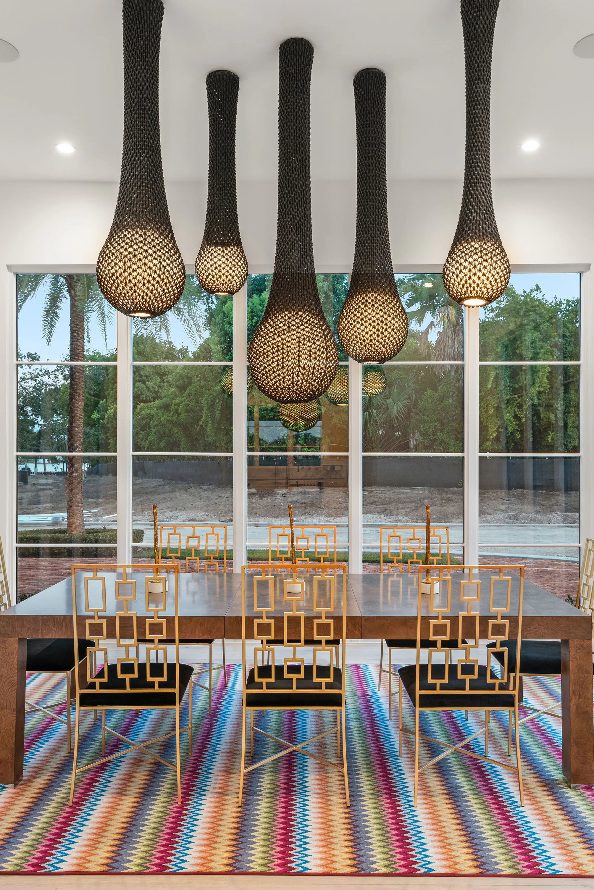 Dark pendant lights suspended above a striped dining rug beside full-height windows.