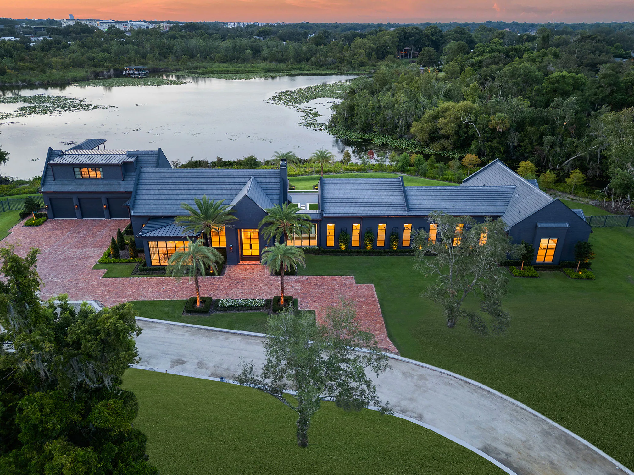 Twilight aerial view over Manor's roofline toward the lake, with warm light in the rear rooms.