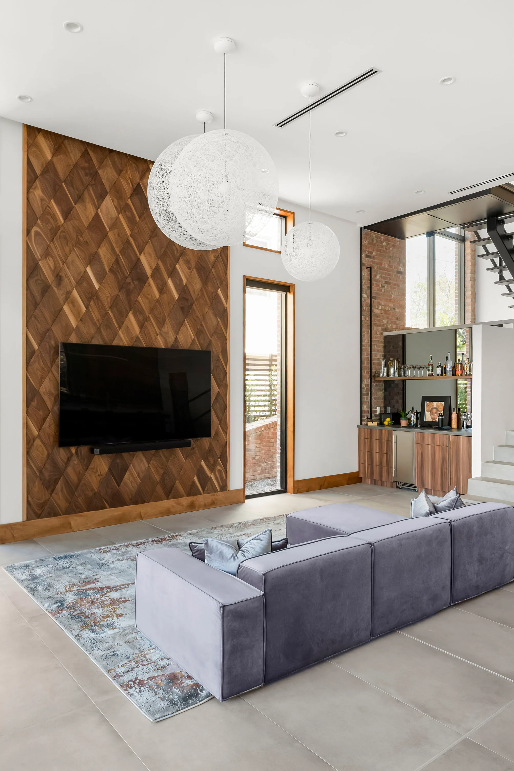 Living room centered on a dark fireplace and wood media wall. Terrace, a custom home by Rare Builders in Orlando.