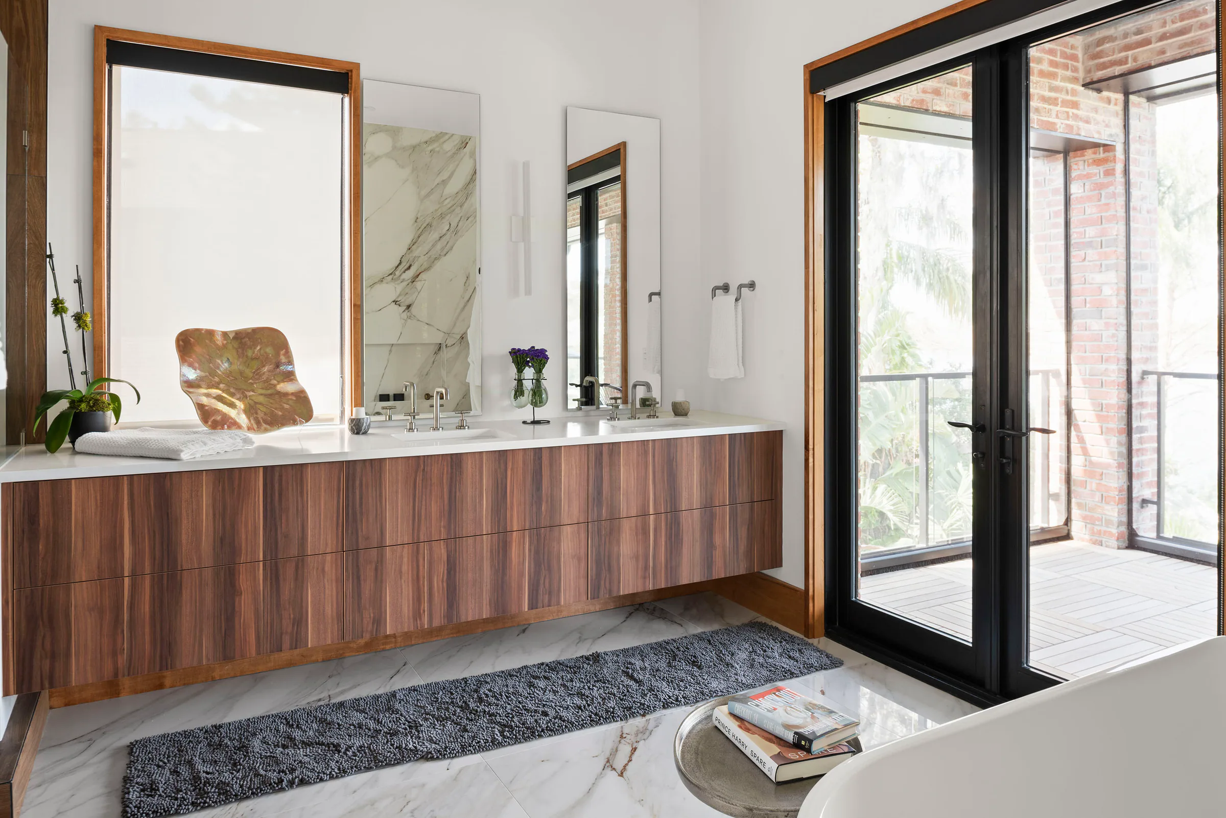 Bathroom with a floating wood vanity, freestanding tub and glazed balcony doors. Terrace, a custom home by Rare Builders in Orlando.