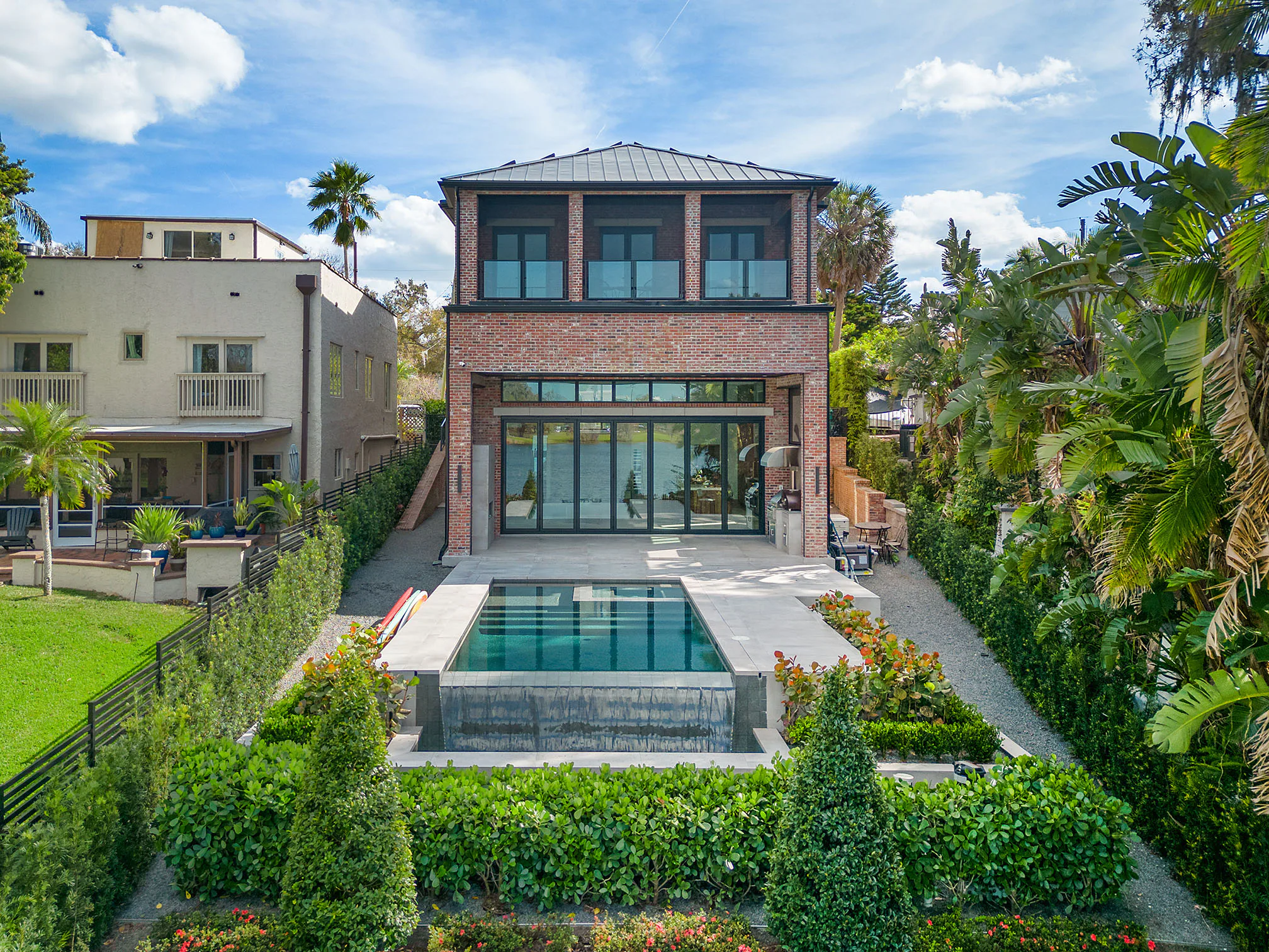 Pool with a spillover edge centred on the rear elevation and clipped hedges. Terrace, a custom home by Rare Builders in Orlando.